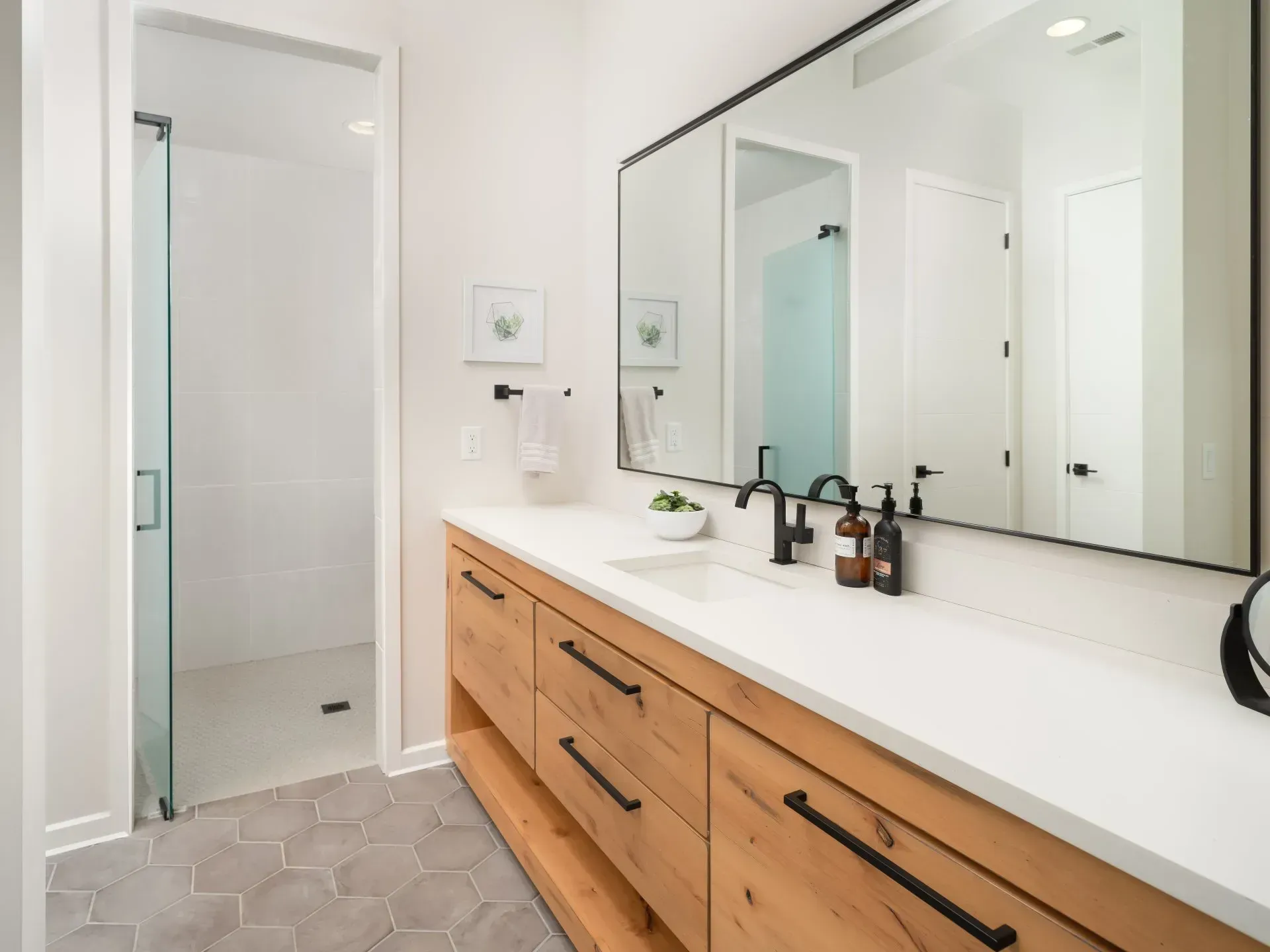 Bathroom with wood vanity, large mirror, white countertop, and glass shower.