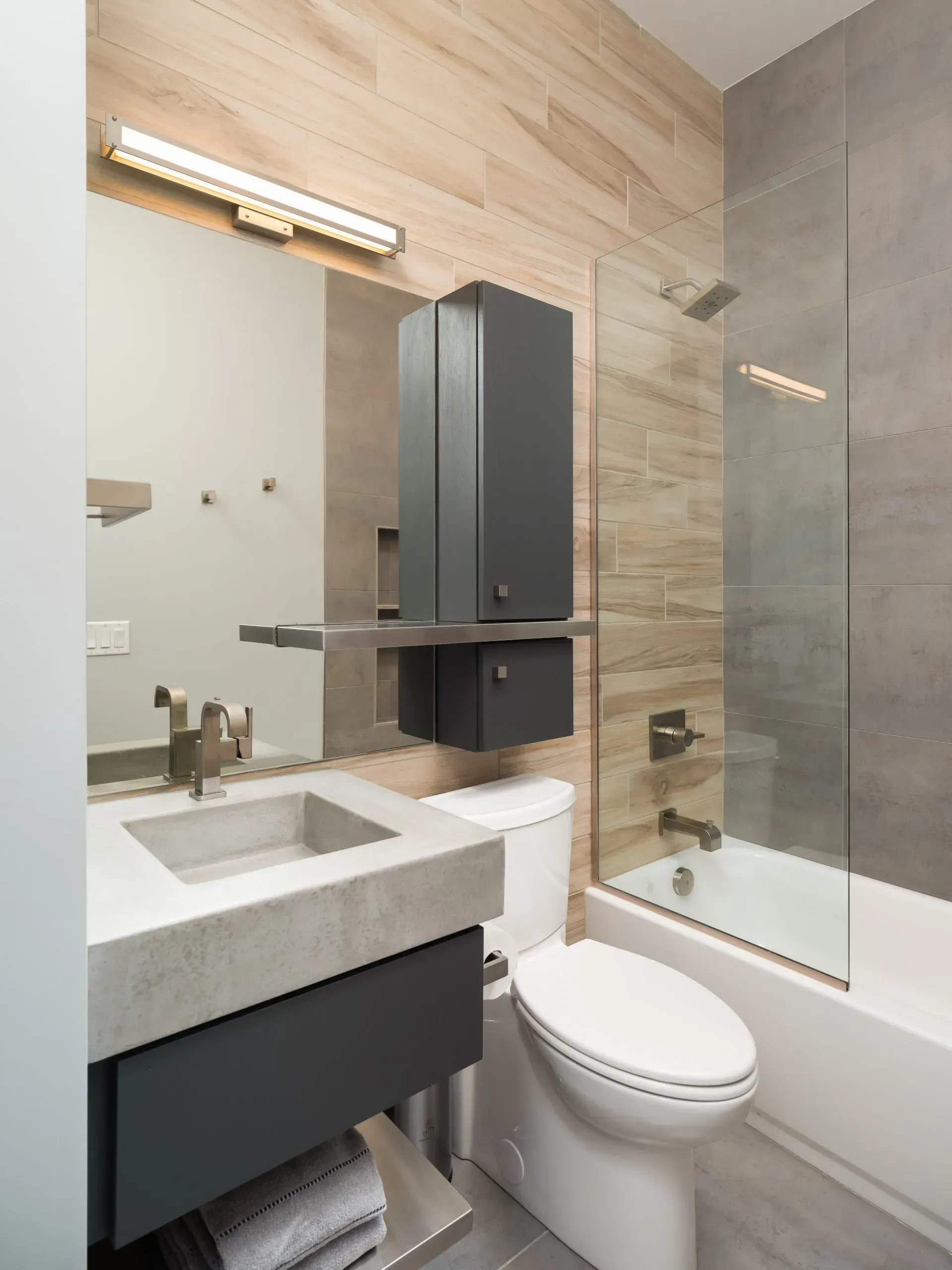 Modern bathroom with gray and wood-tone tiles, concrete sink, dark cabinet, and glass shower screen.