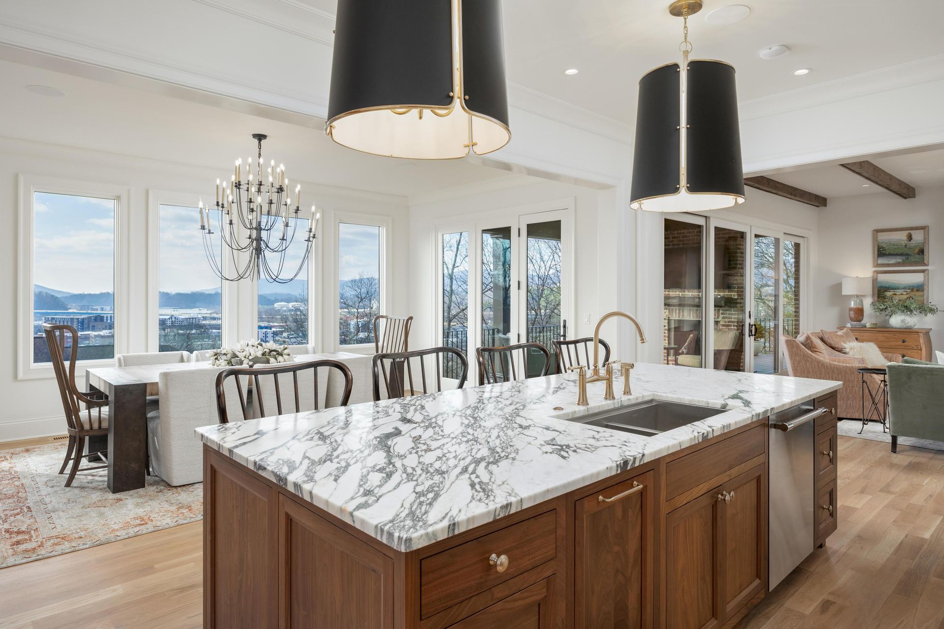 Kitchen with island, dining area with water view, chandeliers, wooden cabinets, marble countertops.