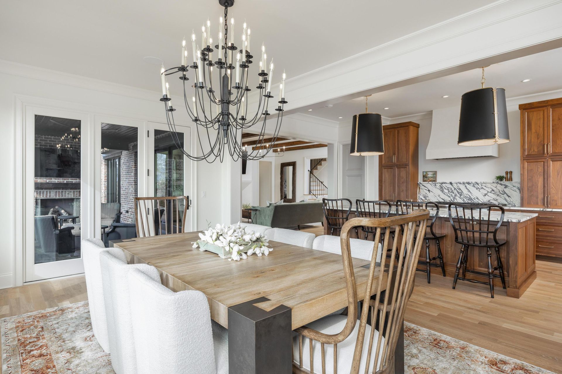 Dining room with a large wooden table, chandelier, and open kitchen with dark cabinets.