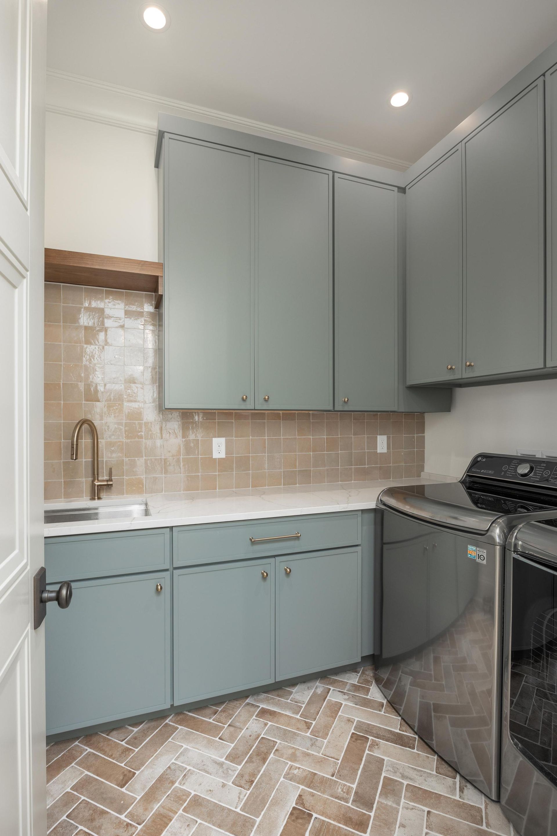 Laundry room with blue cabinets, beige tile backsplash, and herringbone floor. Stainless steel appliances.