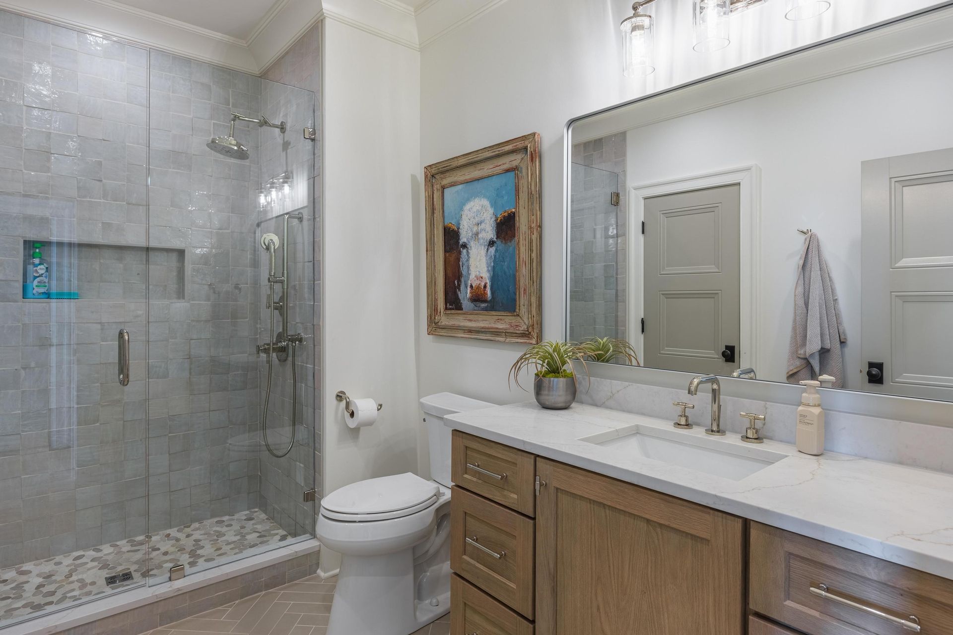 Bathroom with glass shower, toilet, wooden vanity, and artwork.
