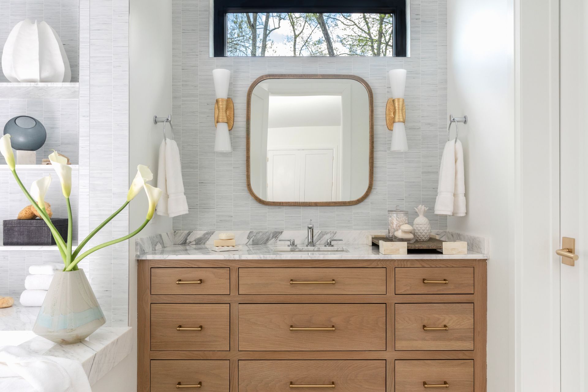 Bathroom with wood vanity, marble countertop, large mirror, and decorative sconces.