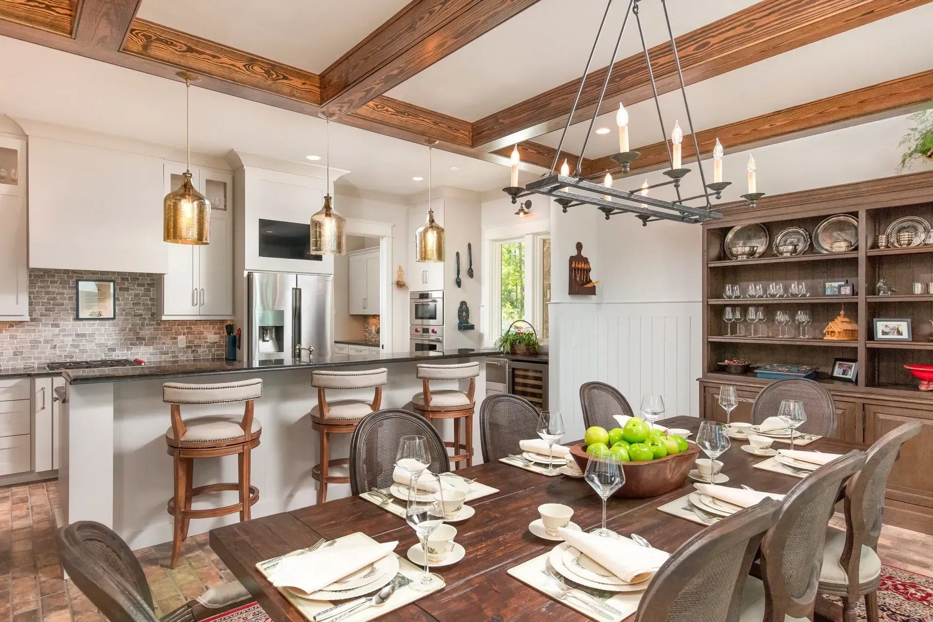 Dining room with table set for a meal, a chandelier, and a kitchen with bar stools.
