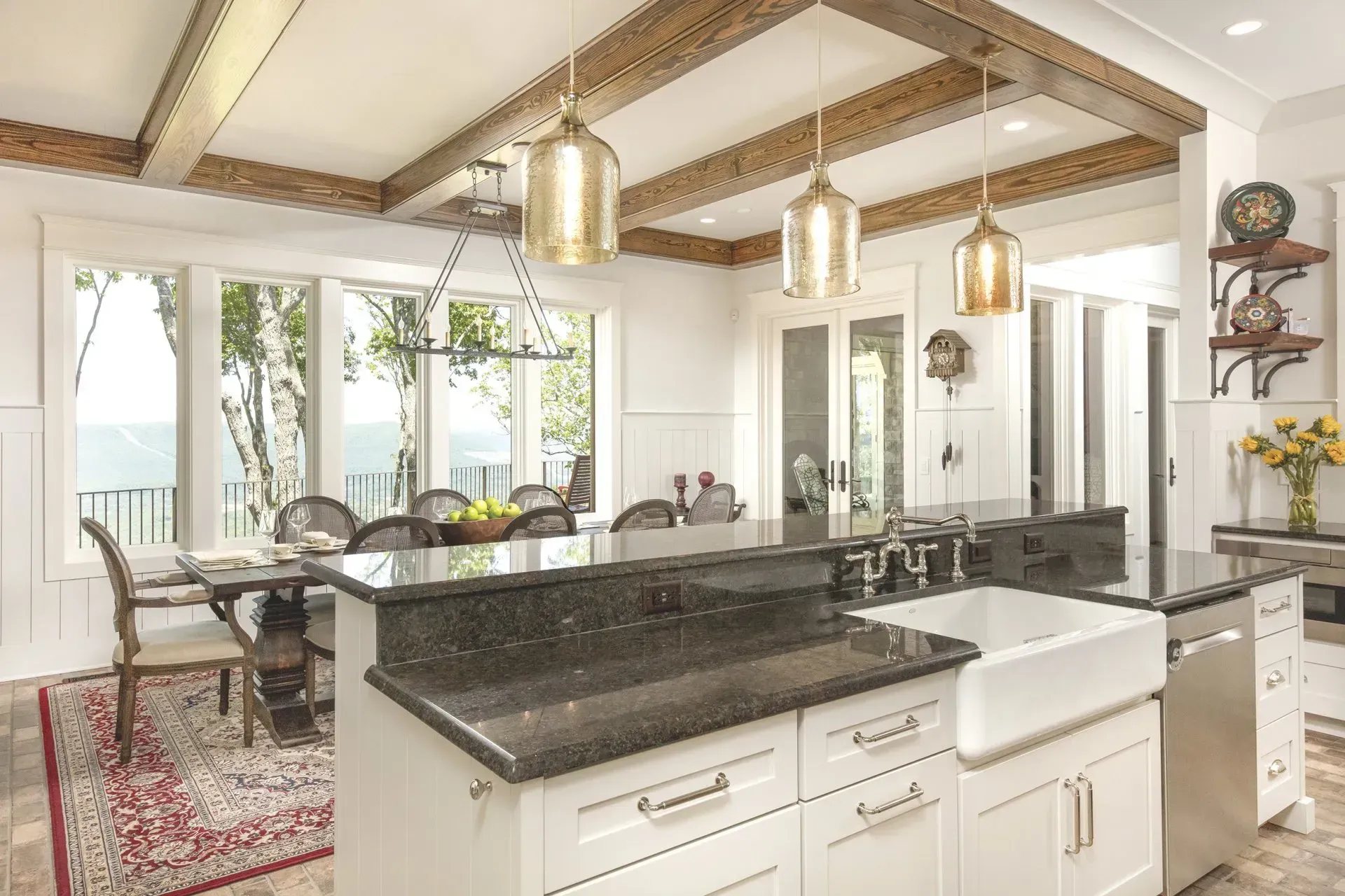 Spacious kitchen with island, white cabinets, dark countertops, and gold pendant lights. Dining area with scenic view.