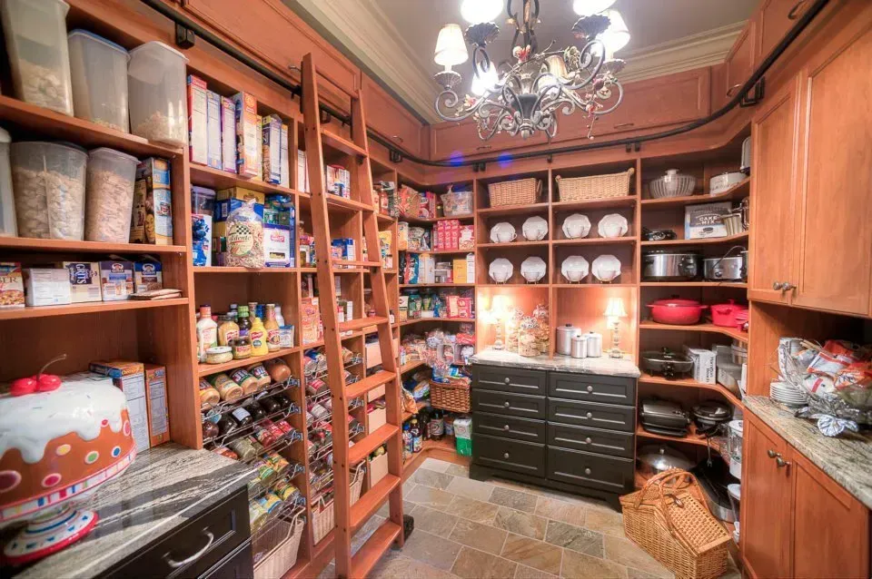 Walk-in pantry filled with wooden shelves and a rolling ladder, stocked with food and appliances.