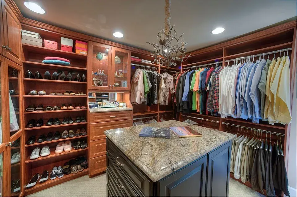 Walk-in closet with brown wood shelves, hanging clothes, shoes, and a central island with a granite top.