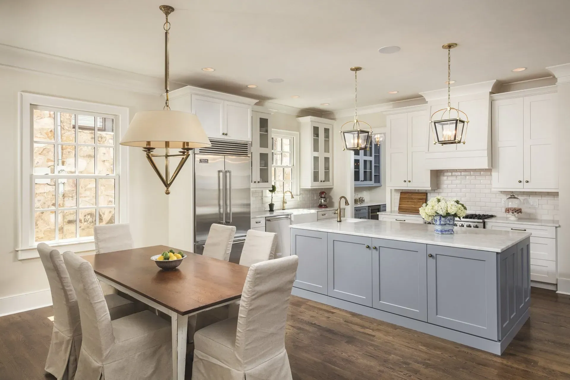 Kitchen with blue island, white cabinets, dining table, and pendant lighting.
