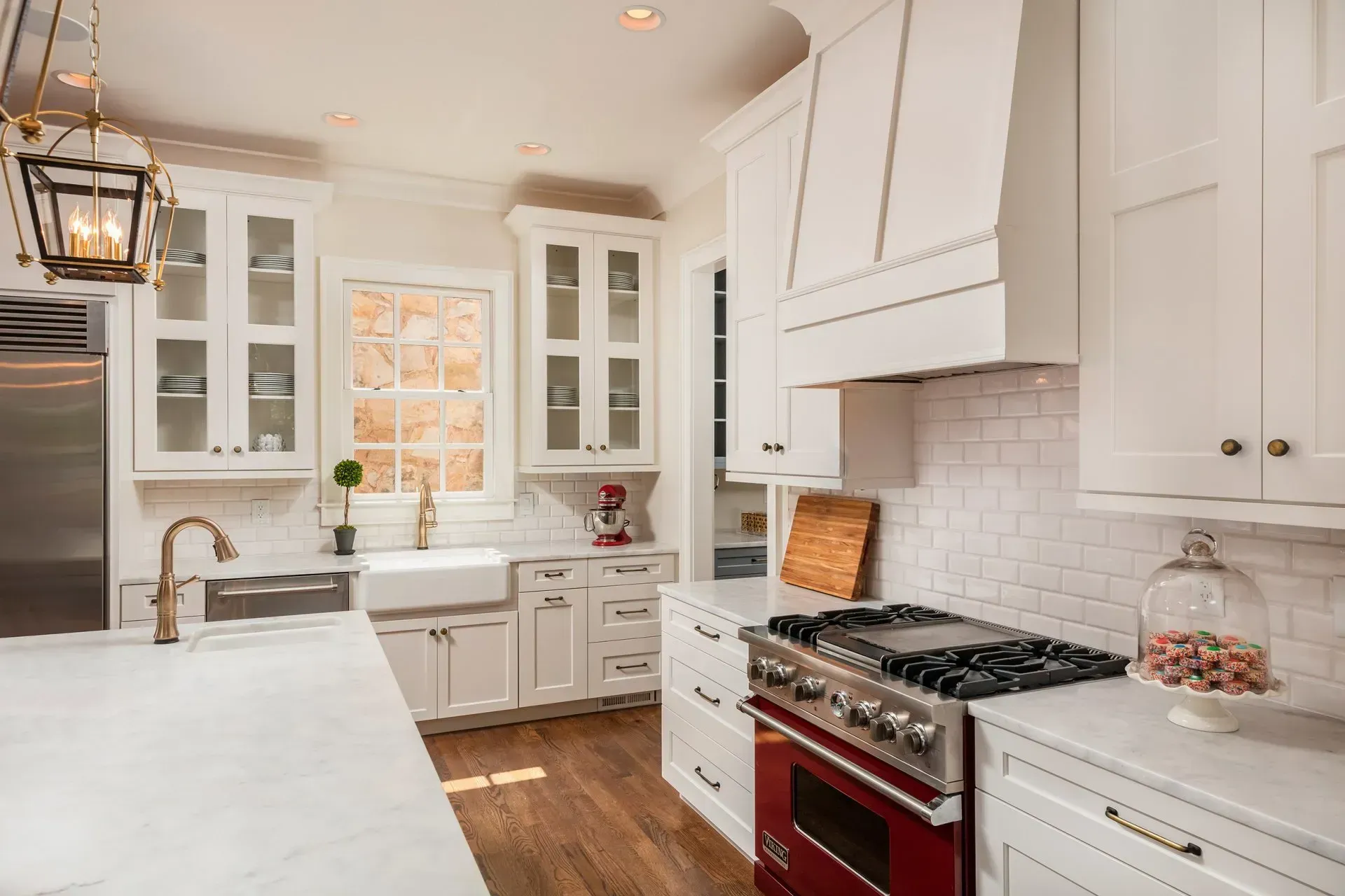White kitchen with red oven, white cabinets, marble countertop, and wood floor.