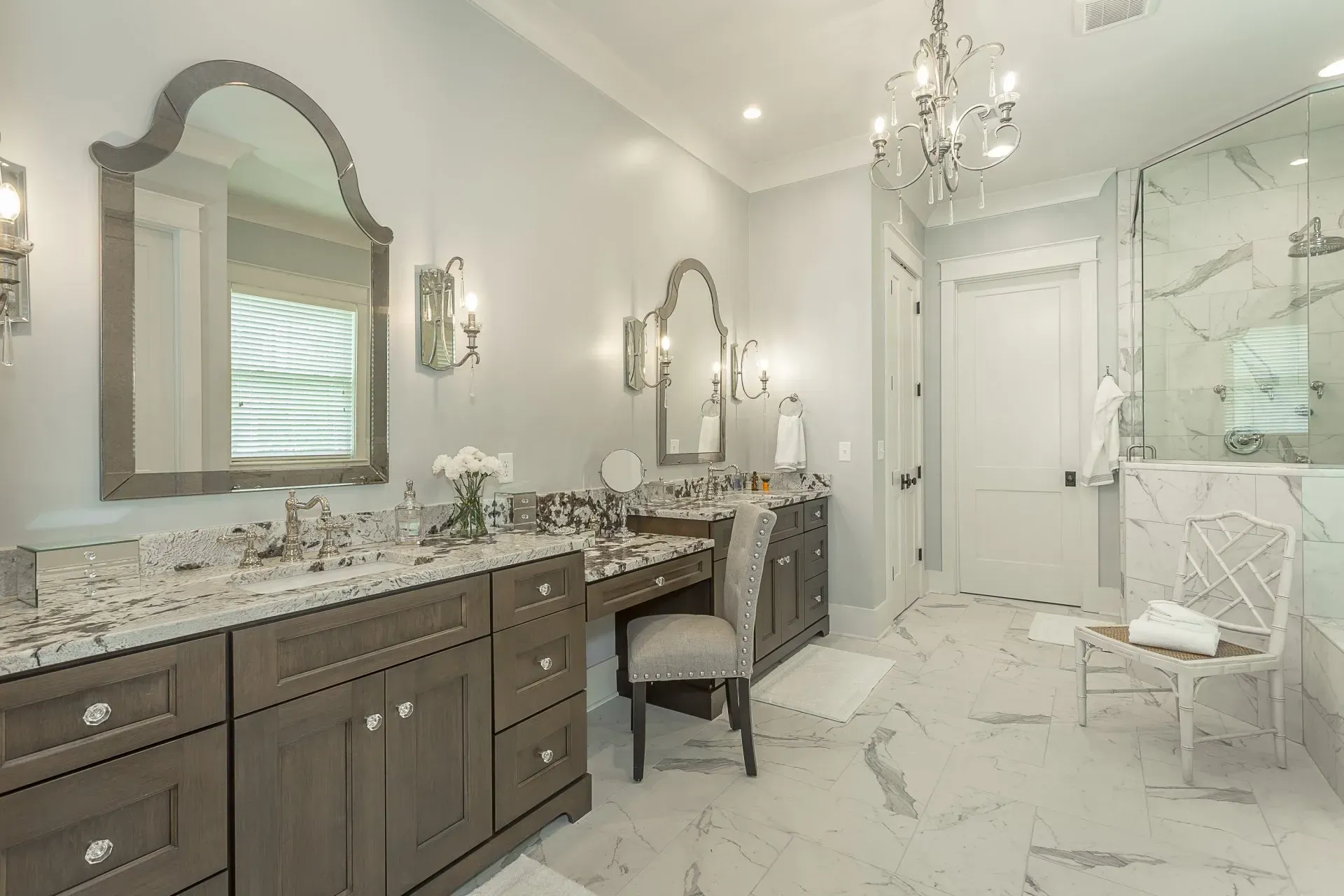 Elegant gray and white bathroom with marble floors, double vanity, and a chandelier.