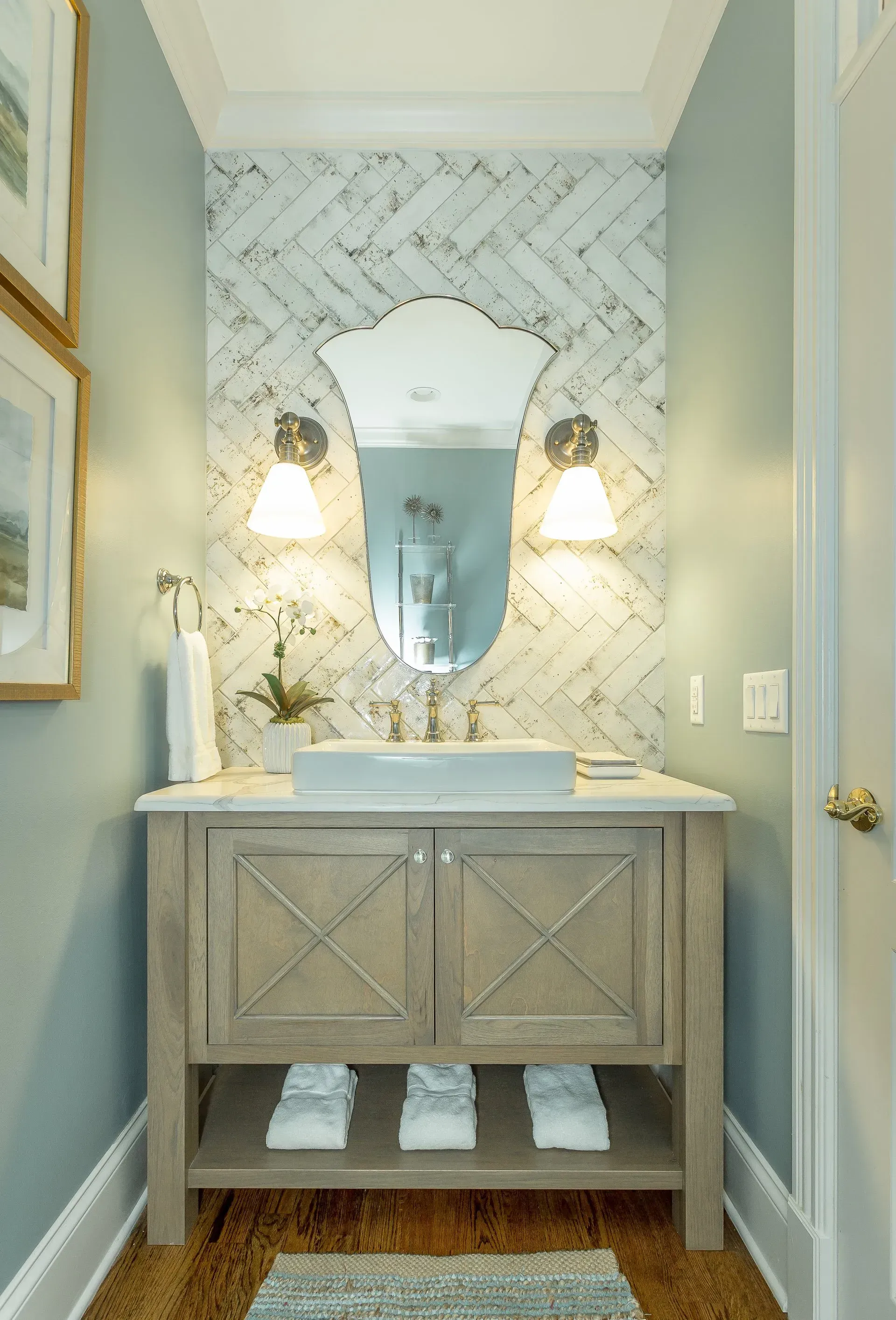 Powder room with light wood vanity, patterned backsplash, oval mirror, and sconces.