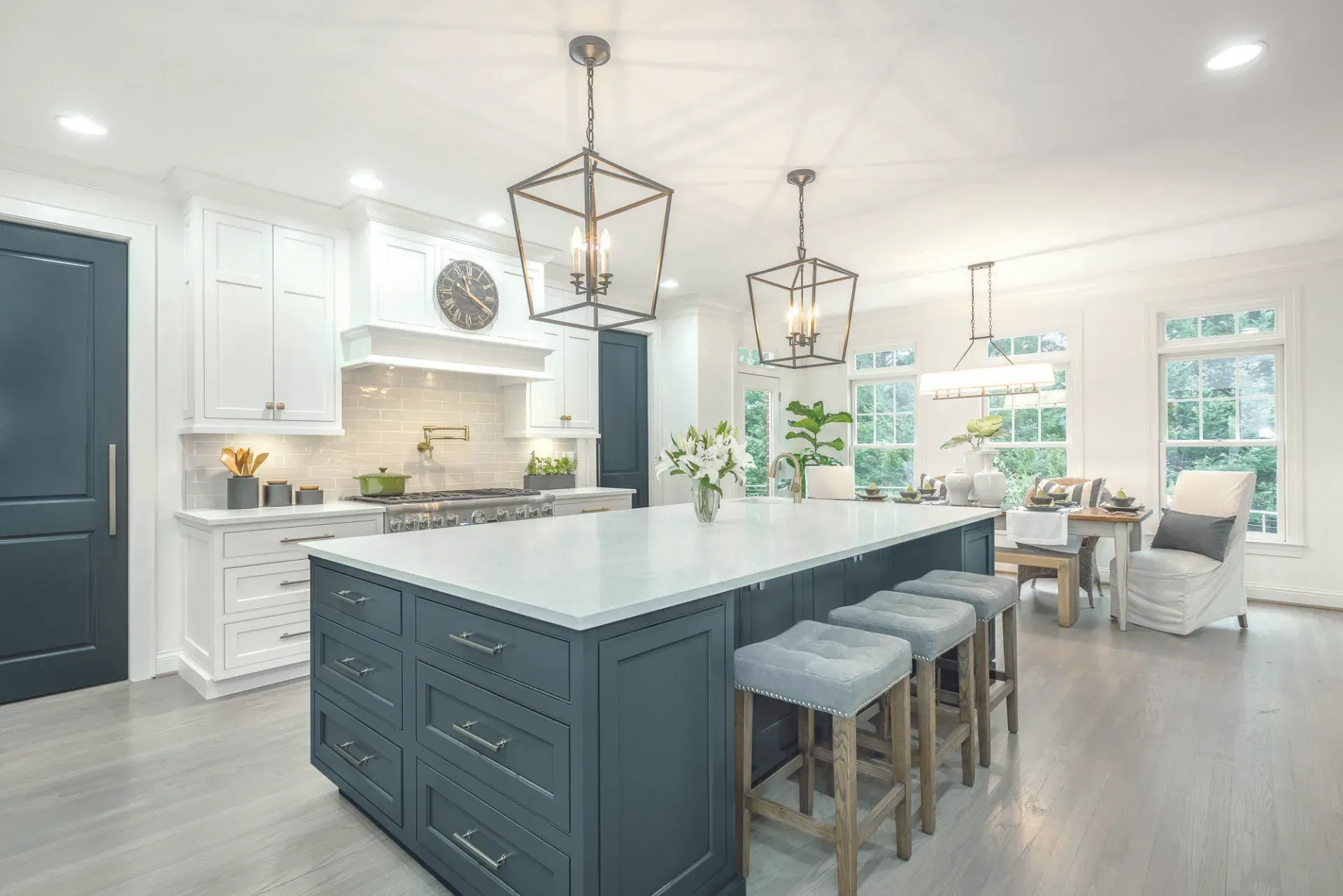 Spacious kitchen with a blue island and white cabinets. Overhead lights, stools, and dining area.