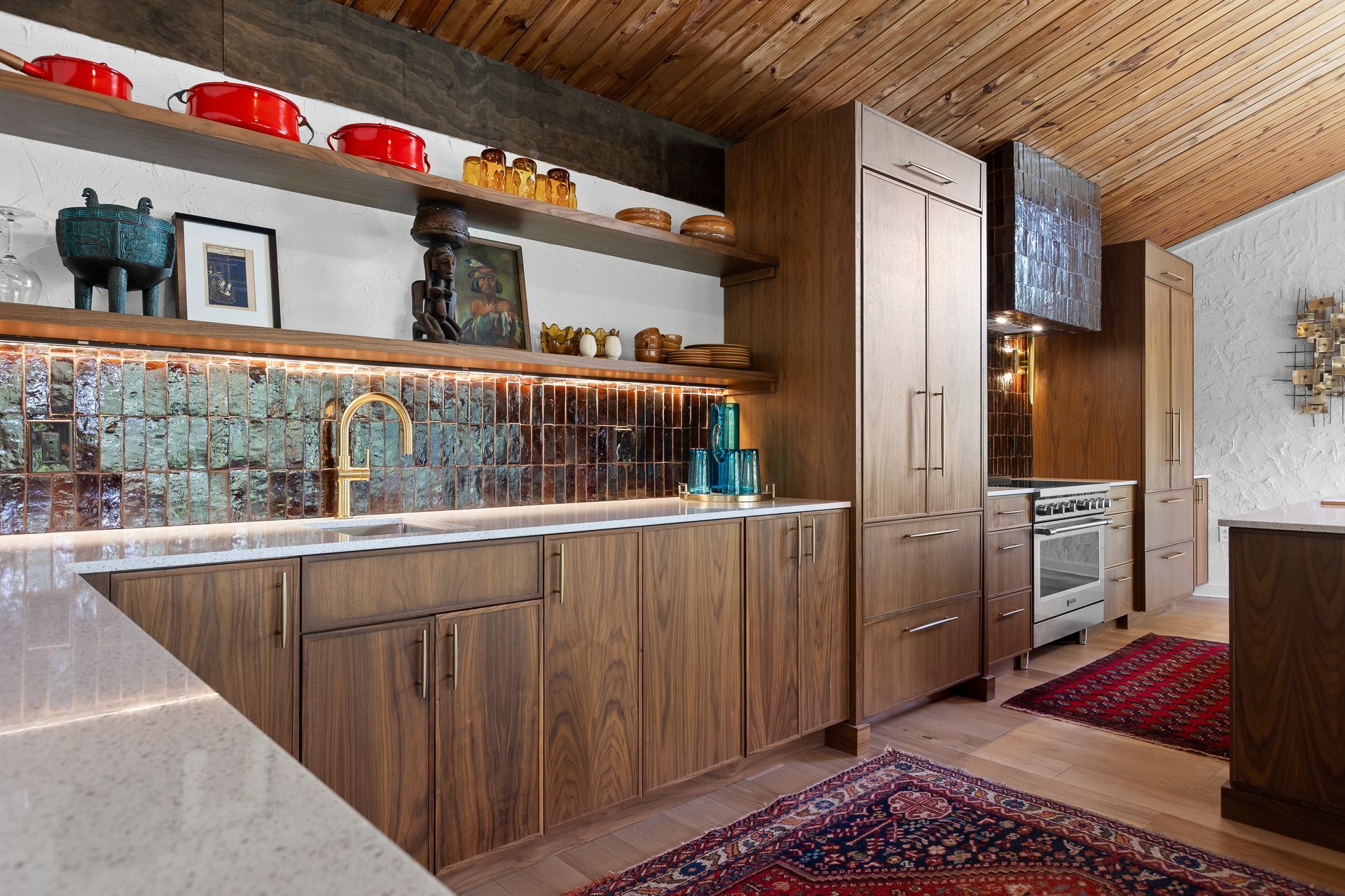 Wooden kitchen with green tiled backsplash, open shelves, and Persian rugs.