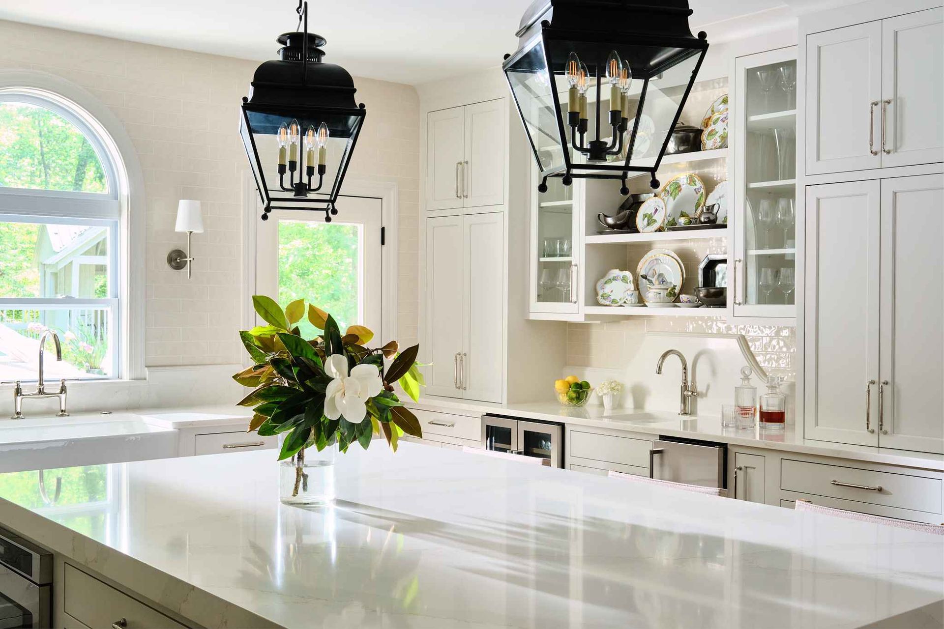 White kitchen with island, black lanterns, window, and flower arrangement.