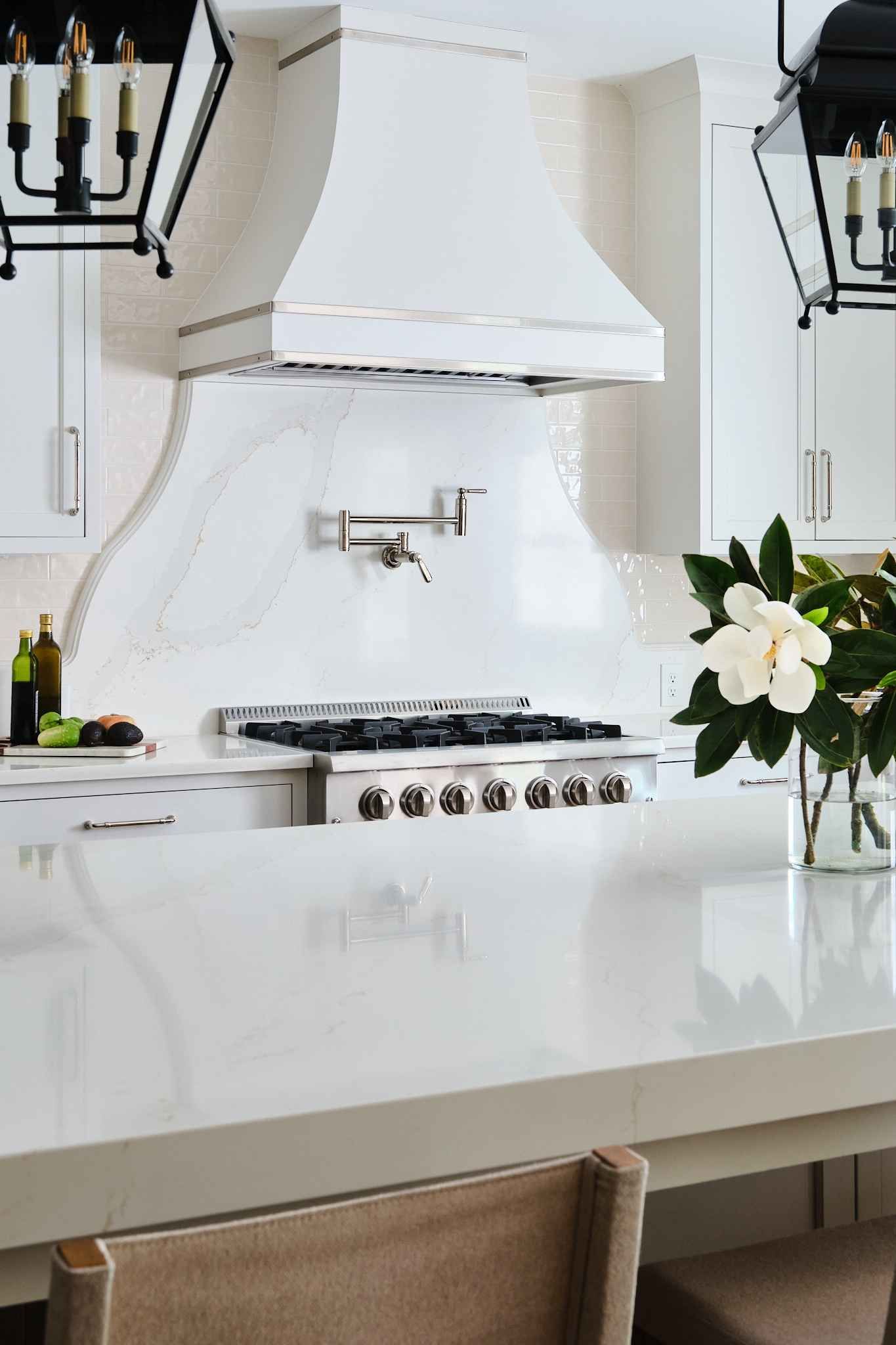White kitchen with range, hood, and countertop, lit by hanging lanterns and flowers.