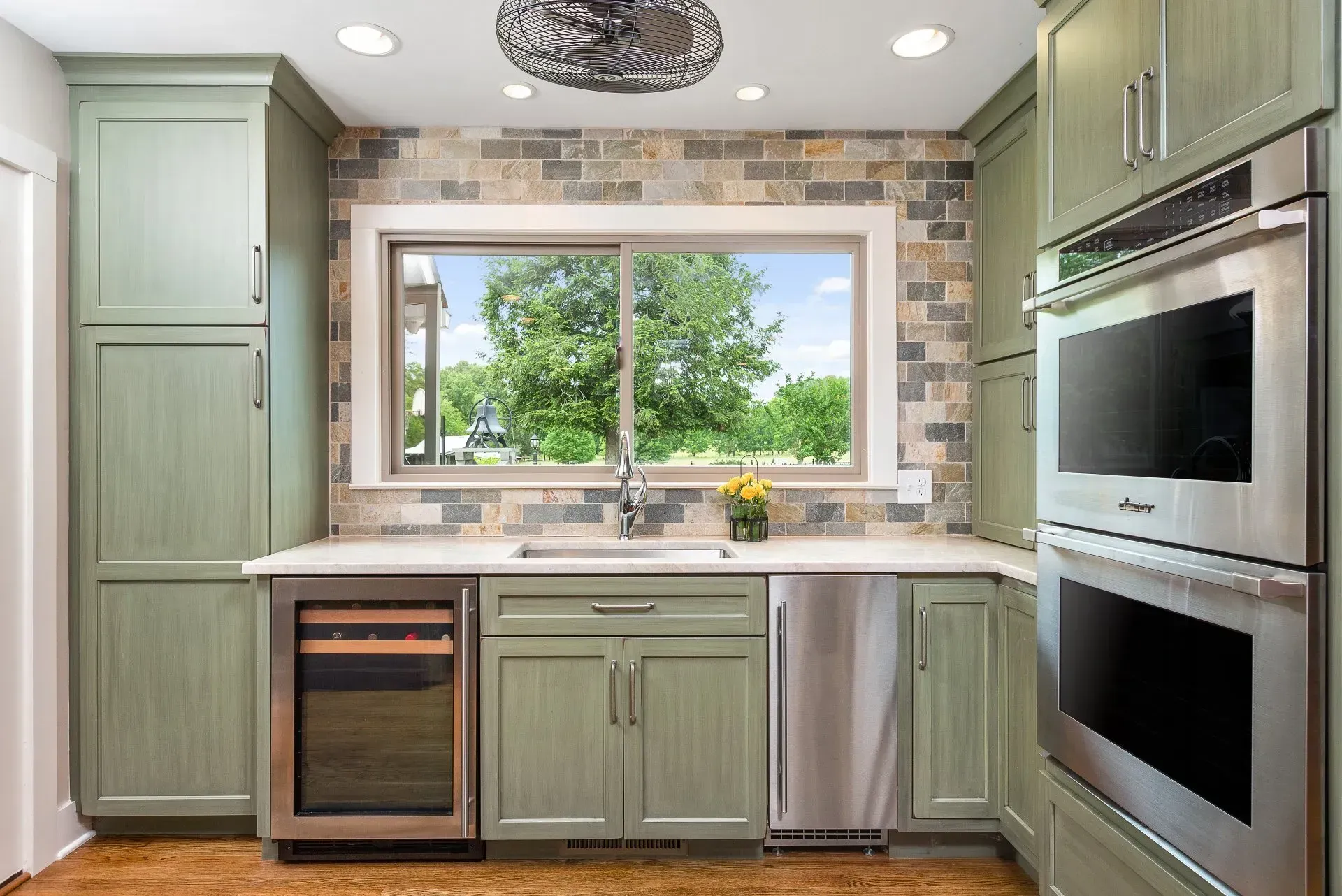 Green kitchen cabinets with a brick backsplash and stainless steel appliances.