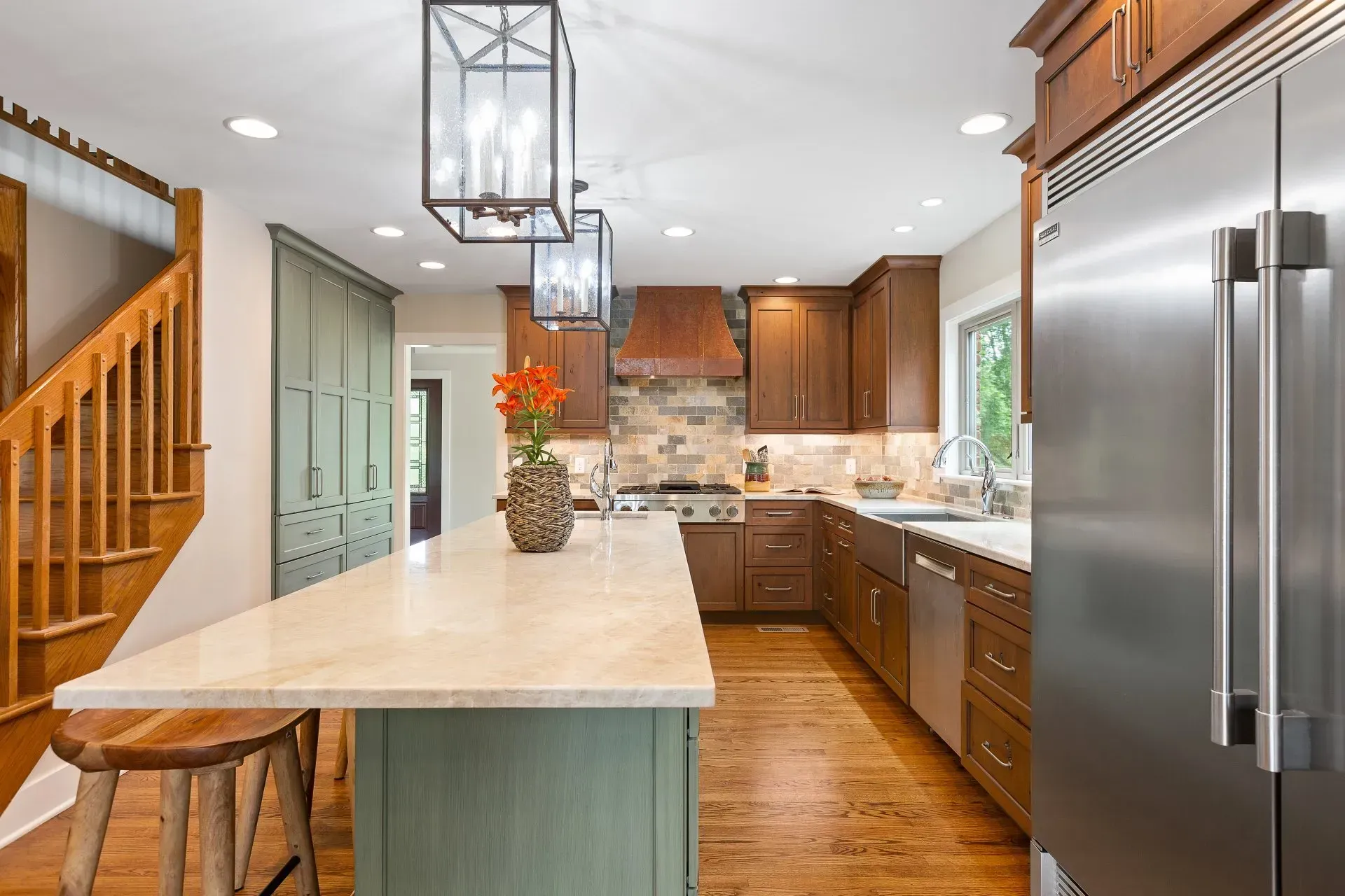 Modern kitchen with wood cabinets, green island, stainless steel appliances, and staircase.