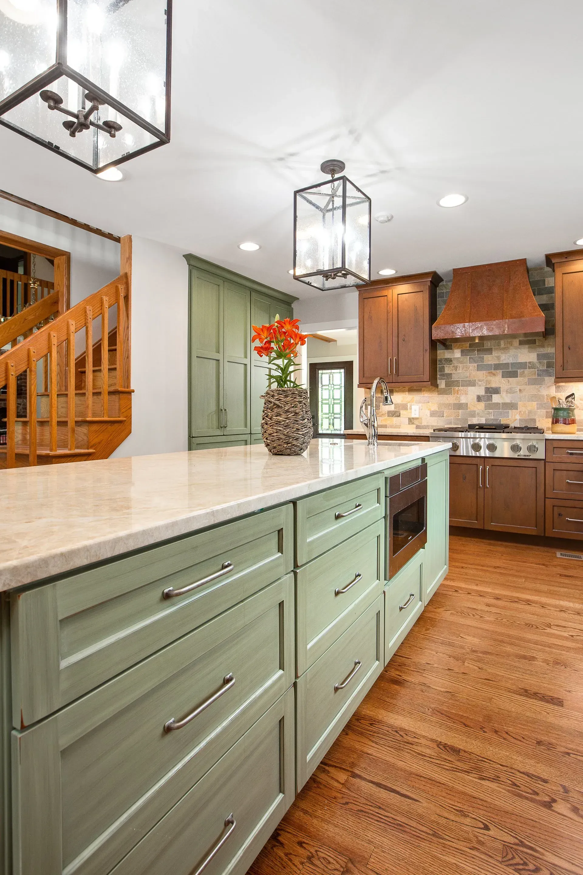 Sage green kitchen island with a light countertop, brown cabinets, and wooden floors.