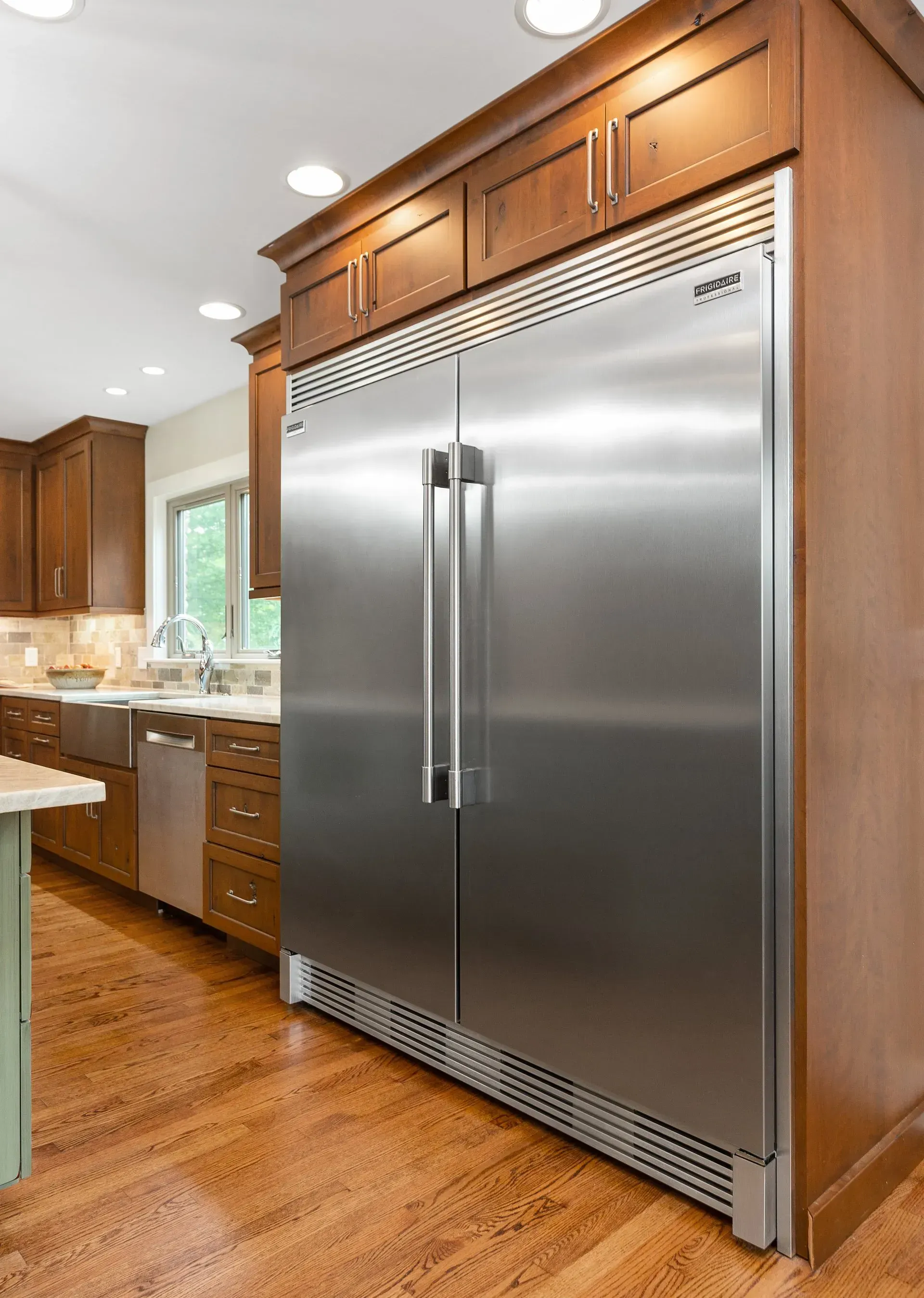 Stainless steel side-by-side refrigerator in a kitchen with wooden cabinets and floors.