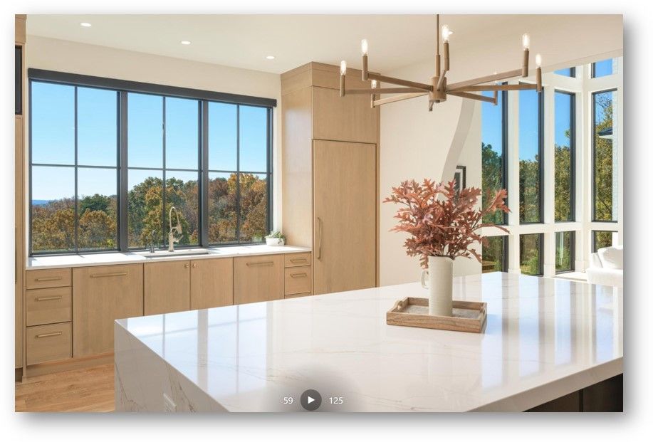 Modern kitchen with large windows, light wood cabinets, and a white countertop island.