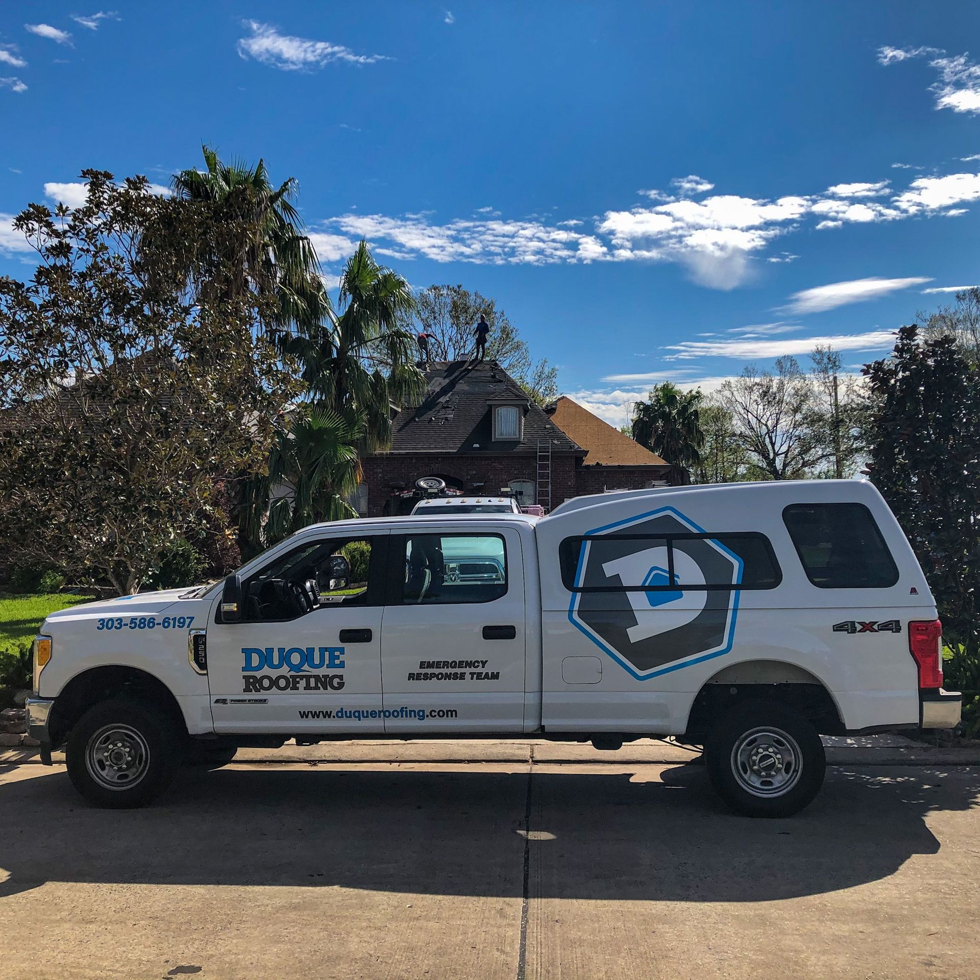 White Duque Roofing truck parked on a street with a house in the background and a blue sky.