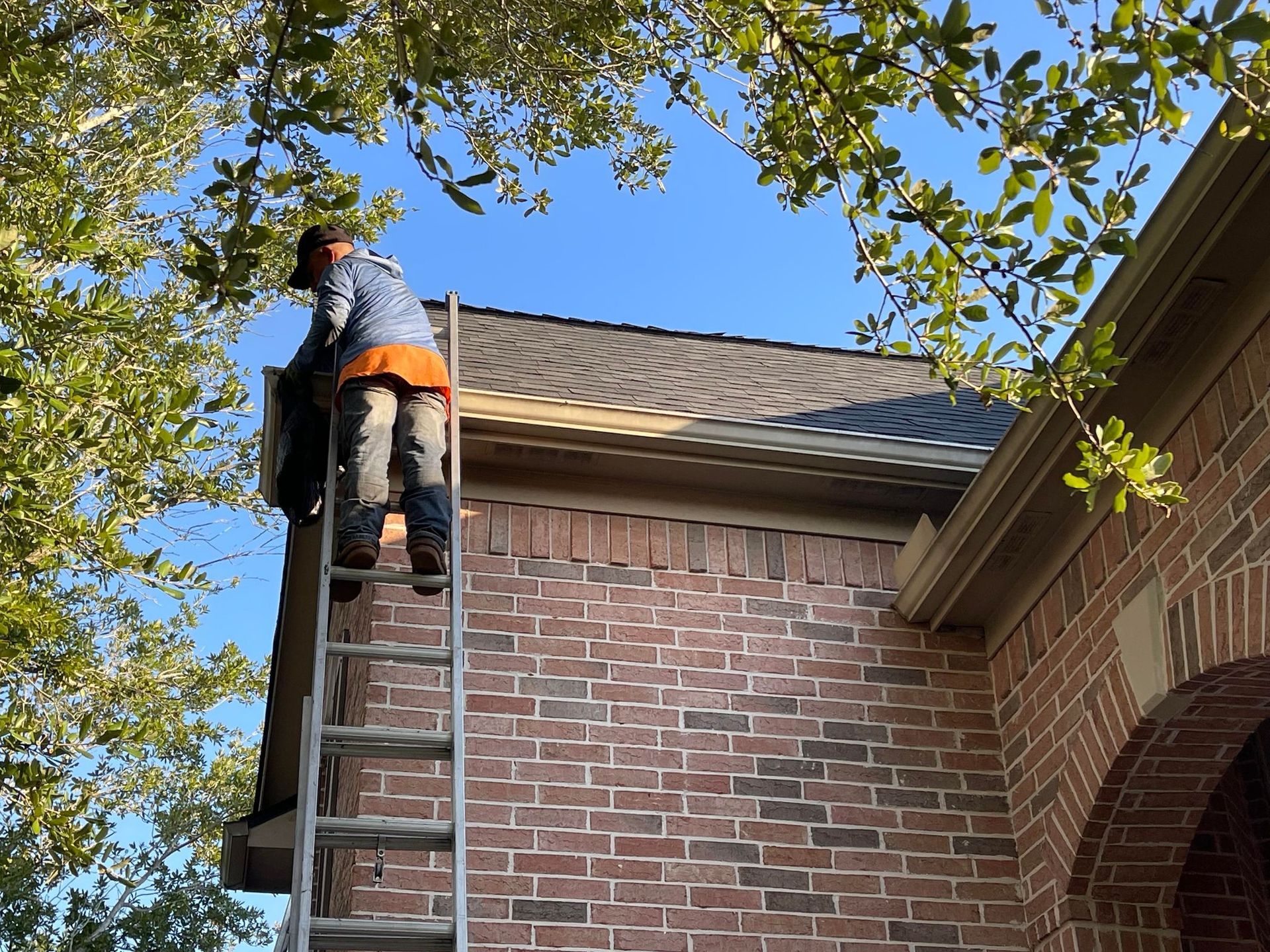 Person on ladder near brick building, installing something on the roof, under blue sky.