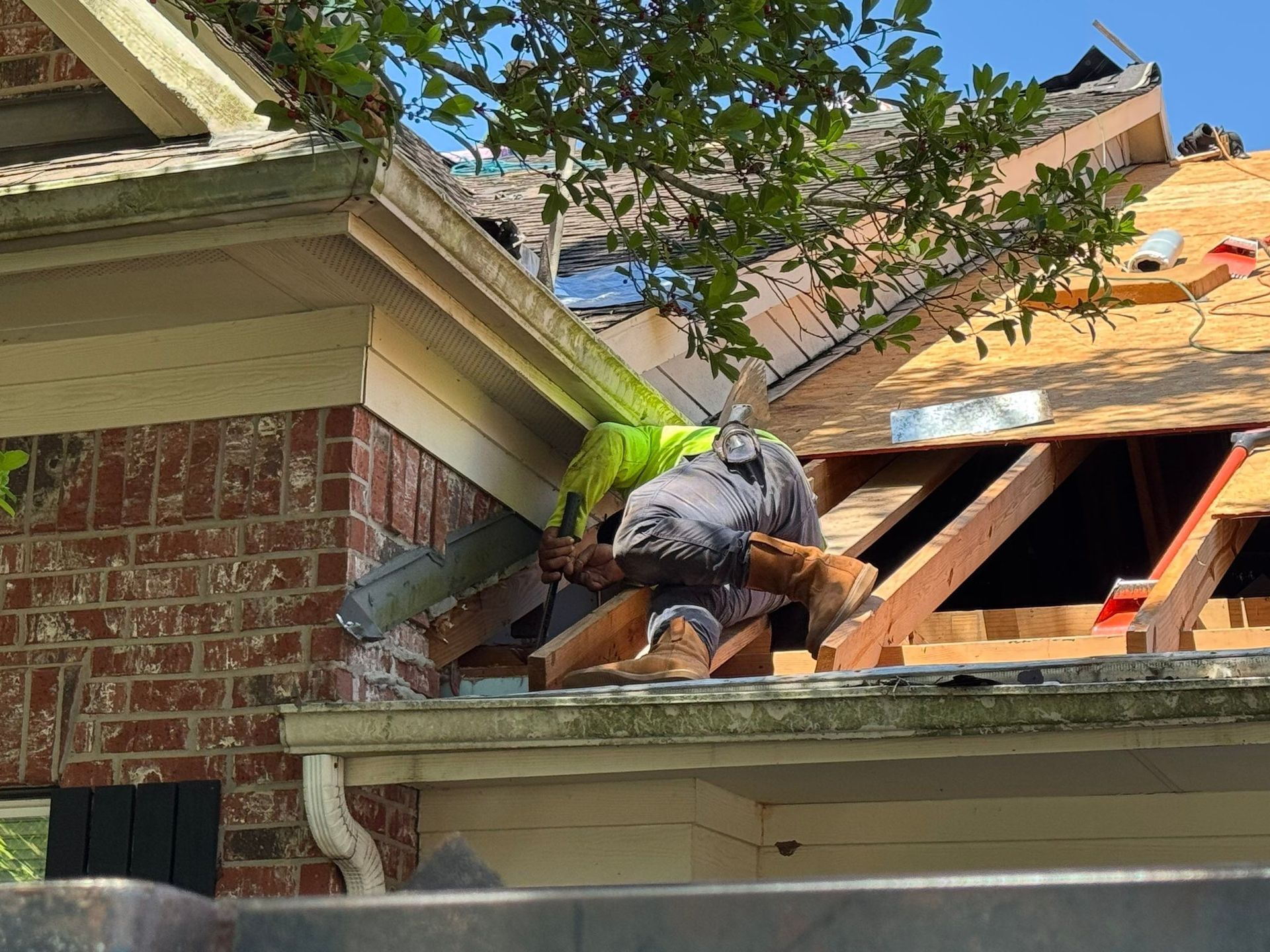 Roofer on a partially demolished roof, working with wood and tools. The structure is brick and wood.