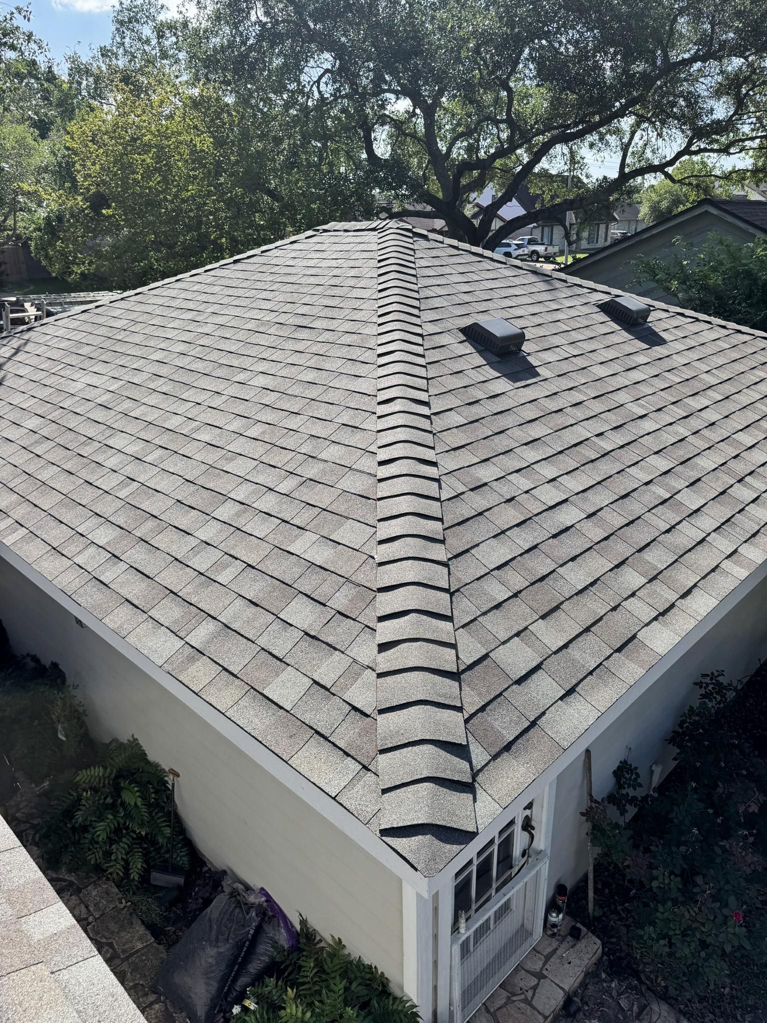 A roof covered in gray shingles with a centered ridge. The house is surrounded by trees.