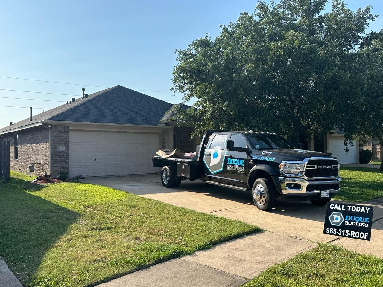 Black work truck parked in front of a house on a sunny day; a sign with a phone number on the lawn.