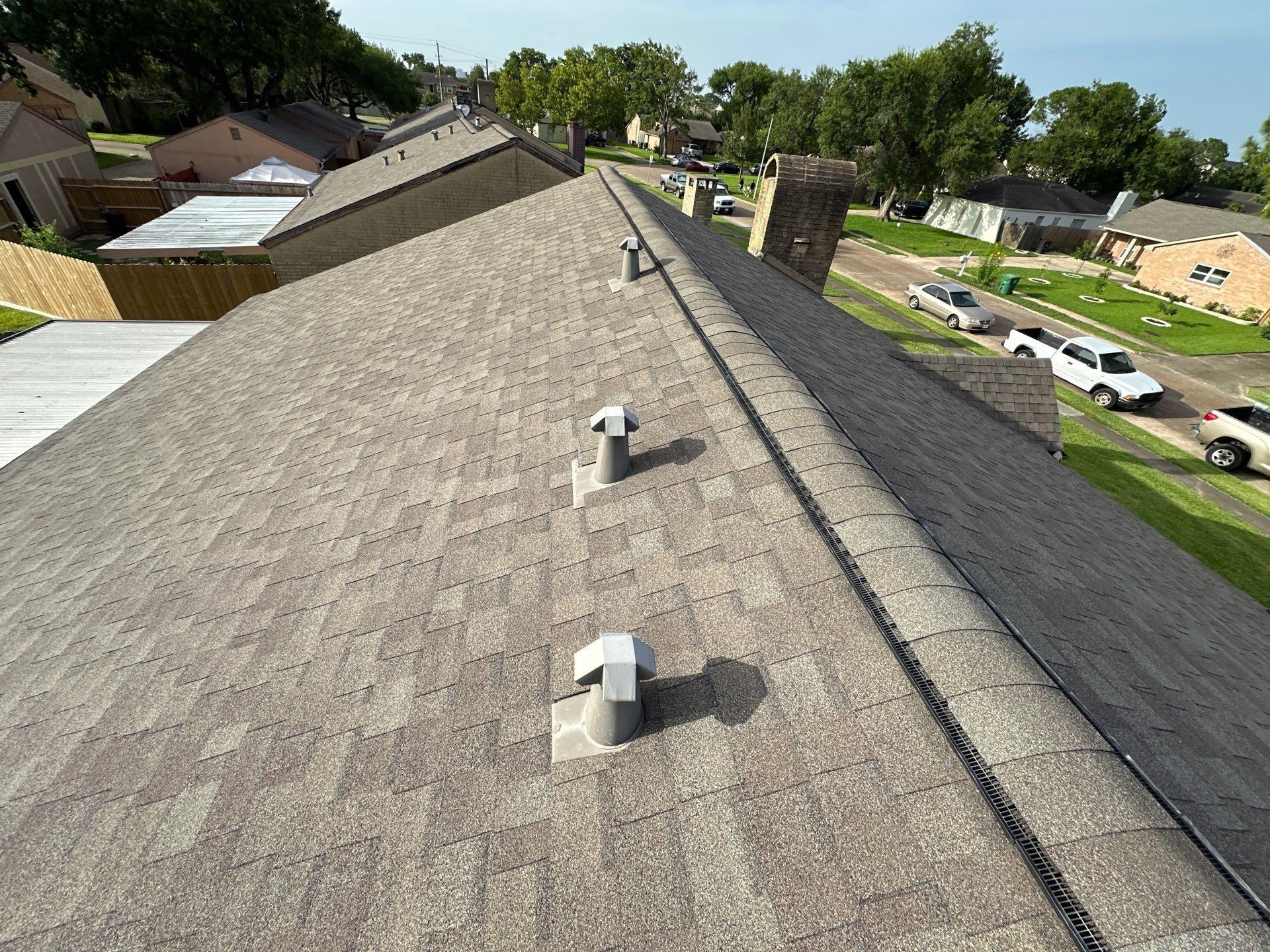 Overhead view of a rooftop with vents, shingles, and surrounding houses on a sunny day.