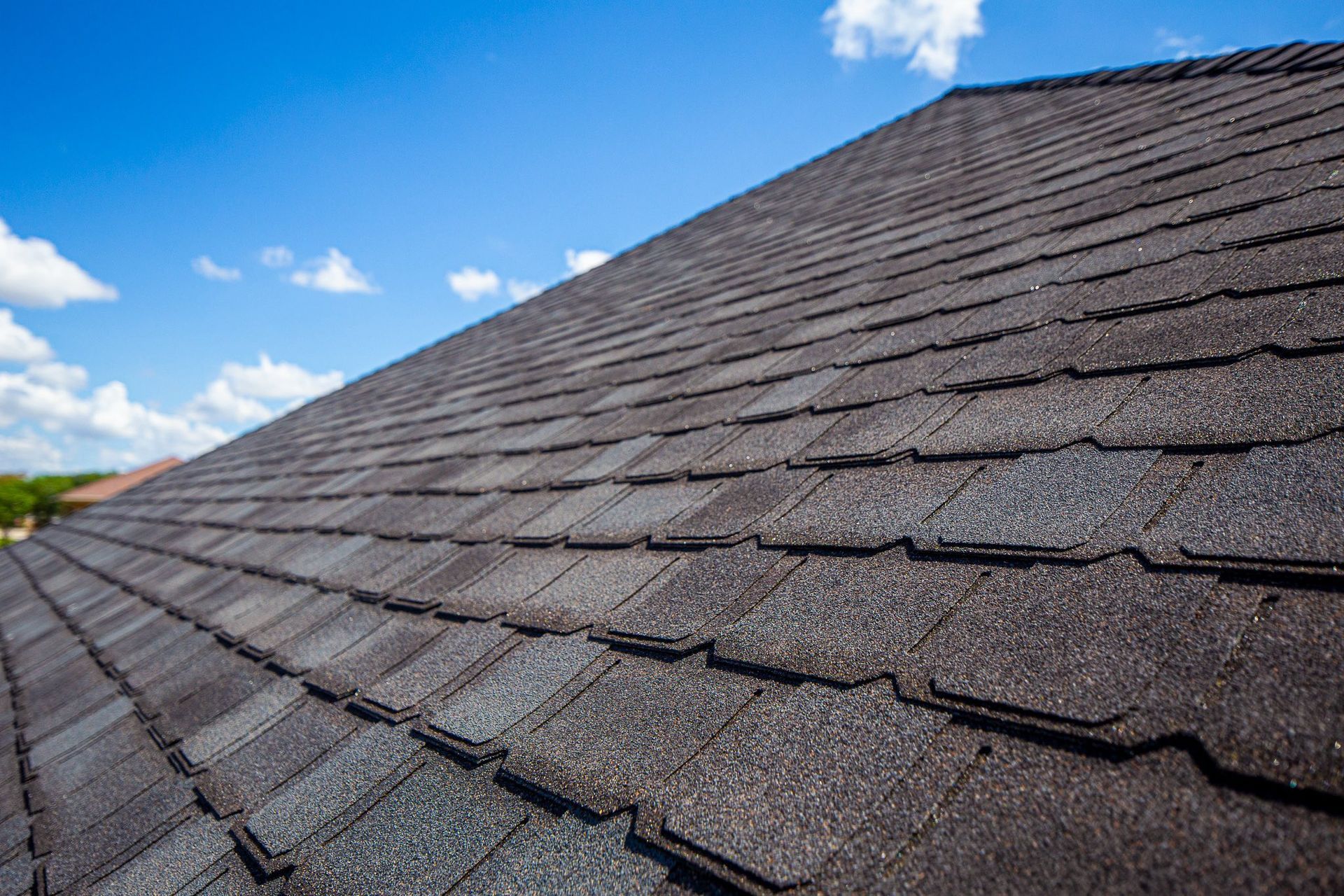 Close-up view of a dark gray composite roof against a blue sky with scattered clouds.