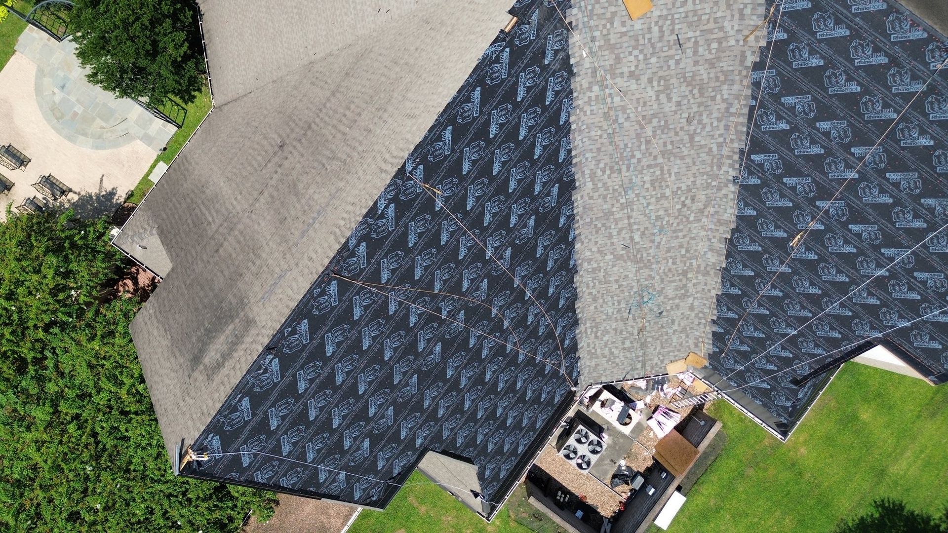 Overhead view of a house roof, some shingles missing, exposing the black underlayment.