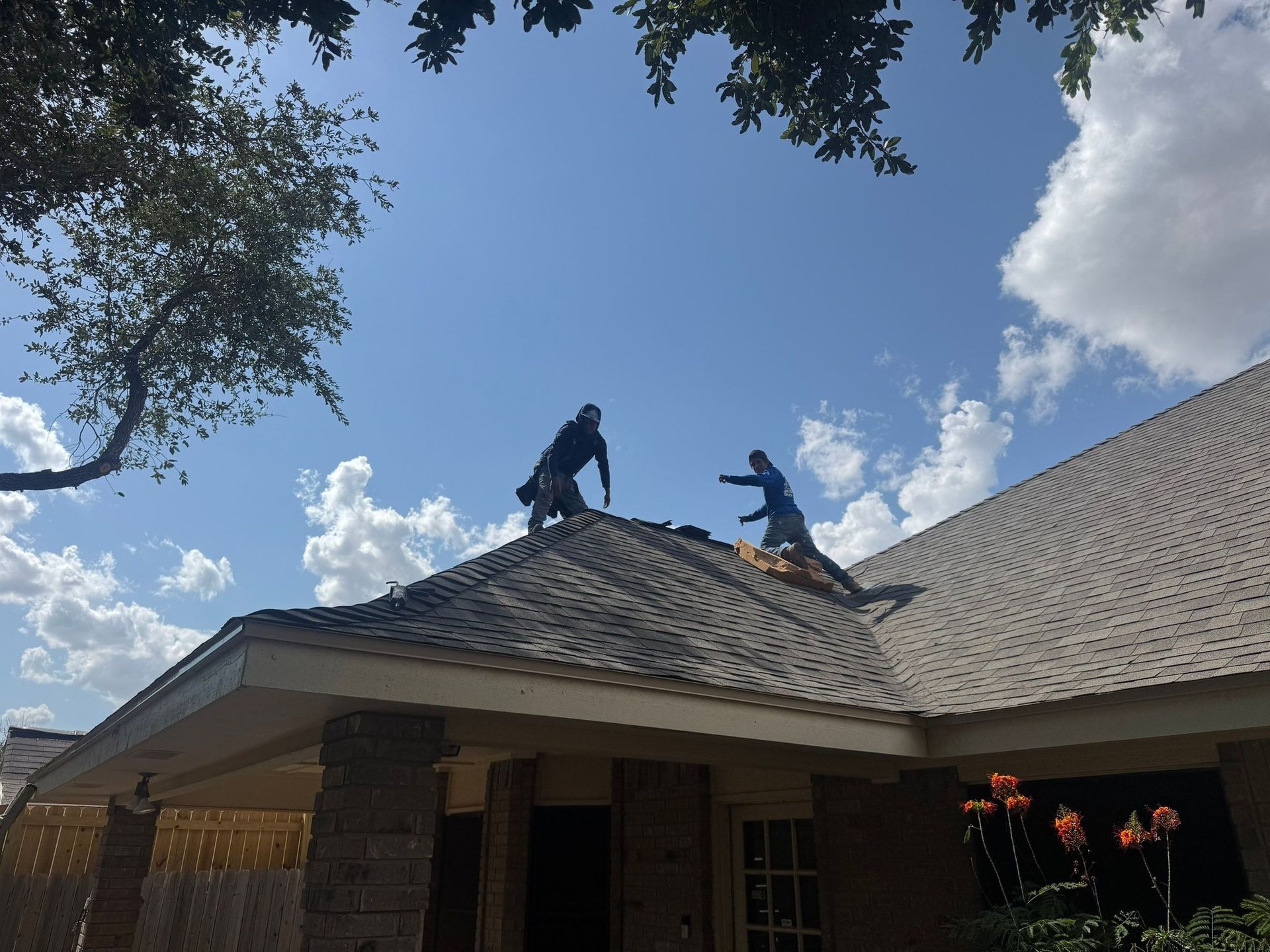 Two roofers on a rooftop under a blue sky with clouds.