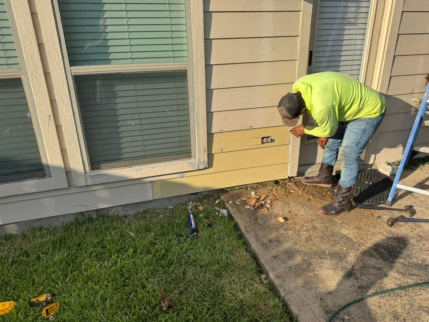 Person in neon shirt working on house siding near a window.