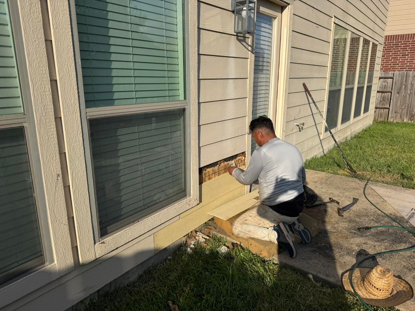 Person working on house siding near a window and door. Exterior shot, sunny day.