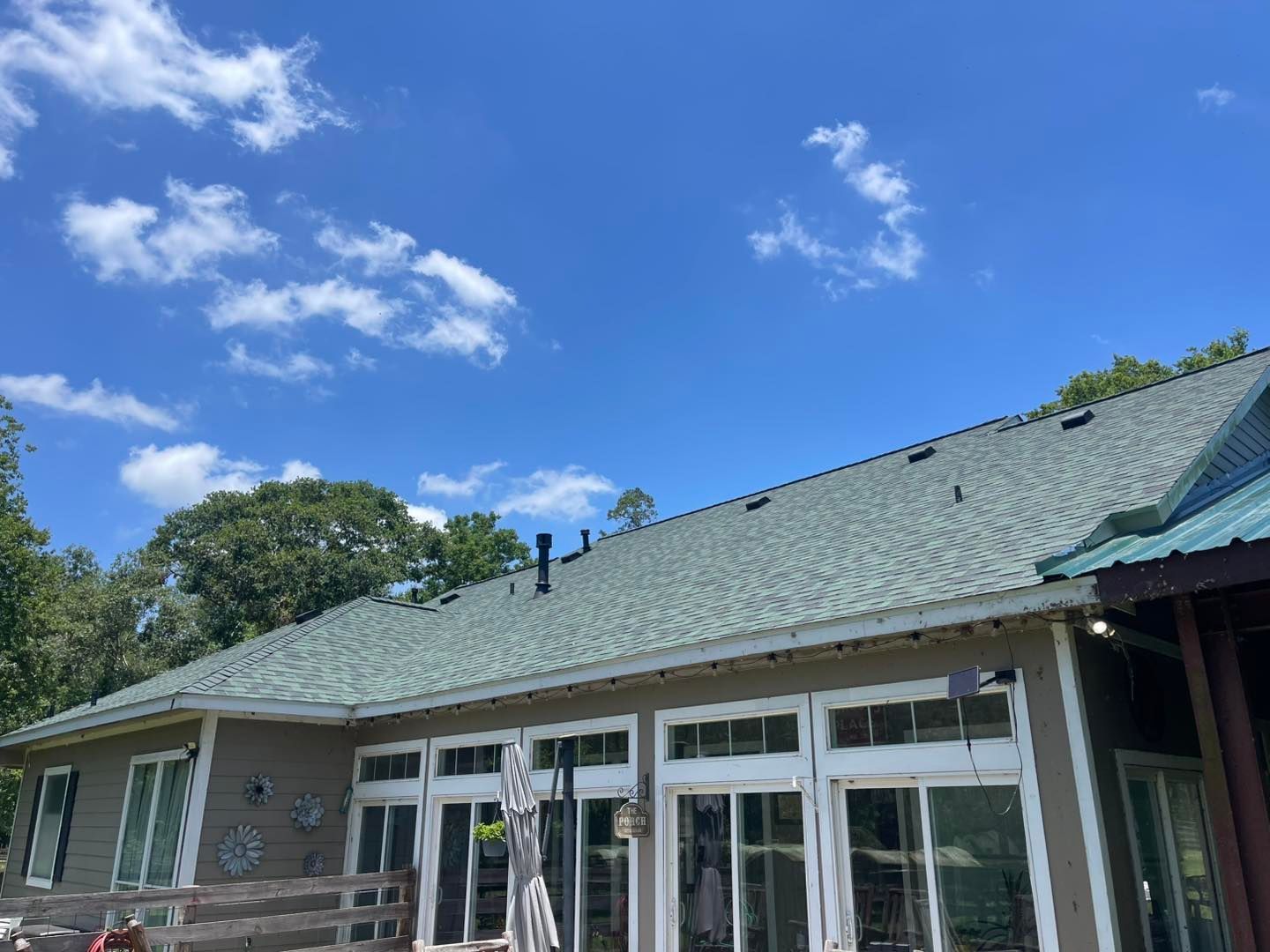 Green-roofed house with white-trimmed windows under a partly cloudy blue sky. Trees are visible in the background.