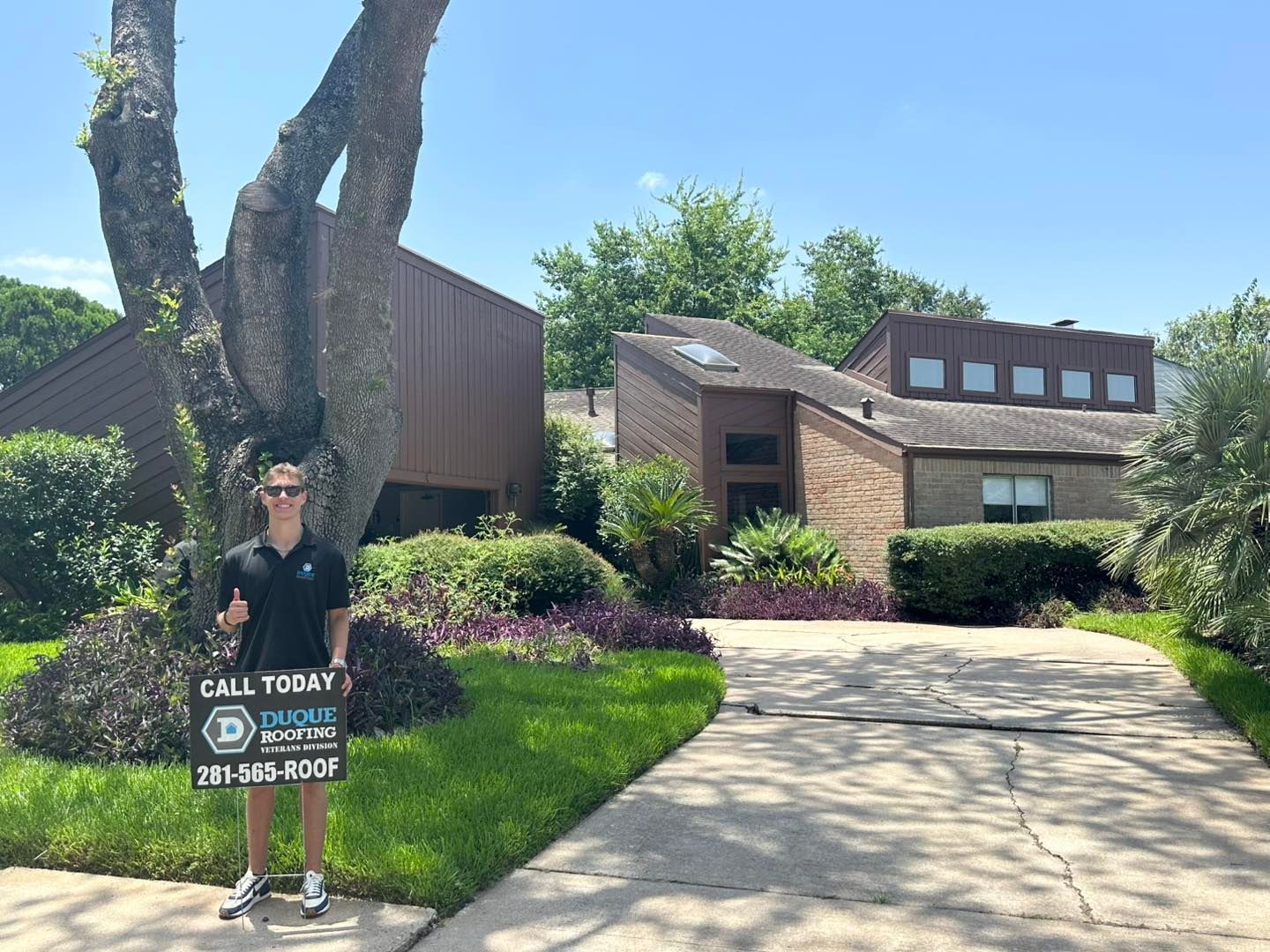 Man holding sign in front of a house. Sign promotes roofing service. Green lawn, blue sky.