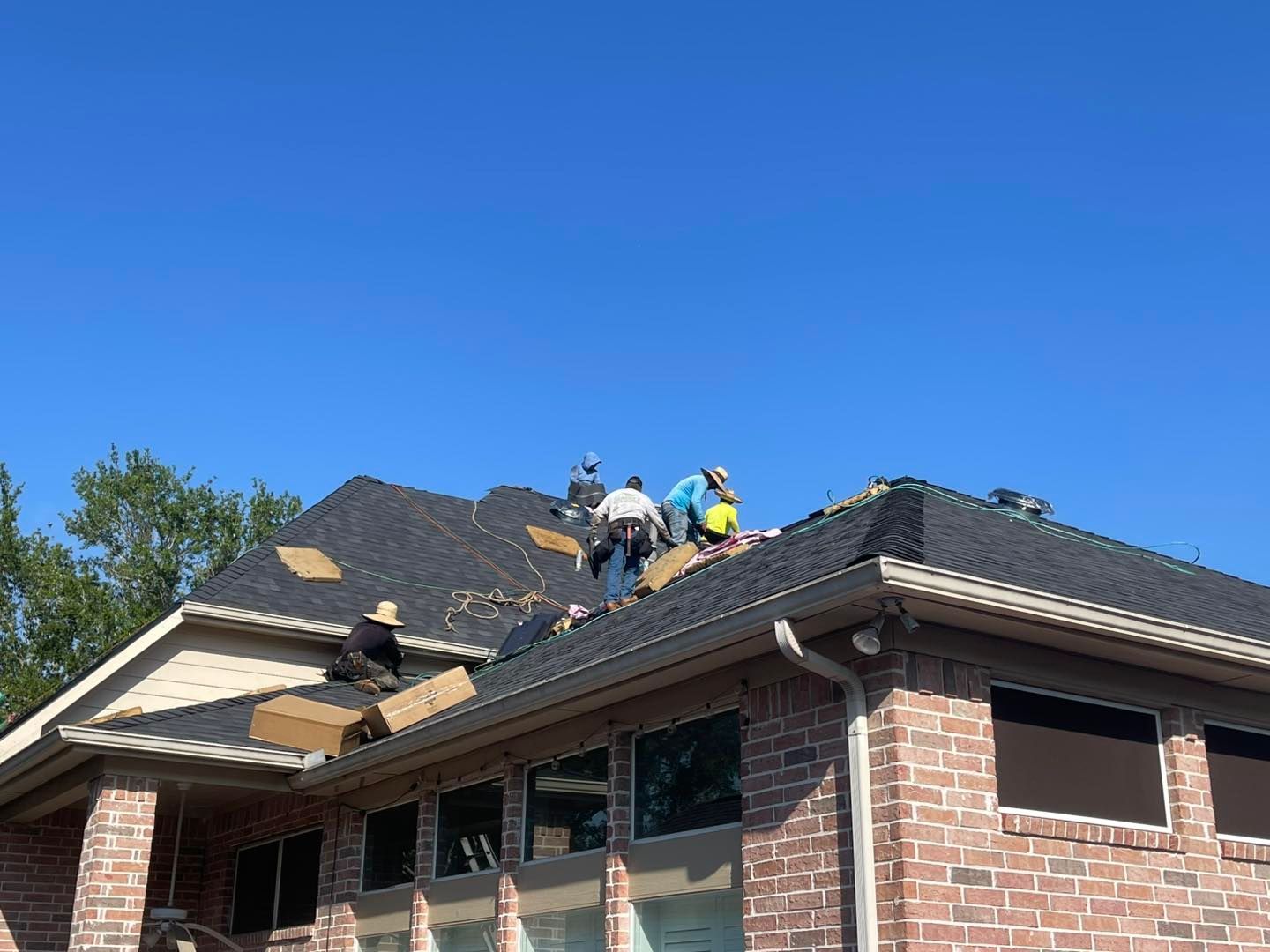 Roofers installing shingles on a brick house under a blue sky.