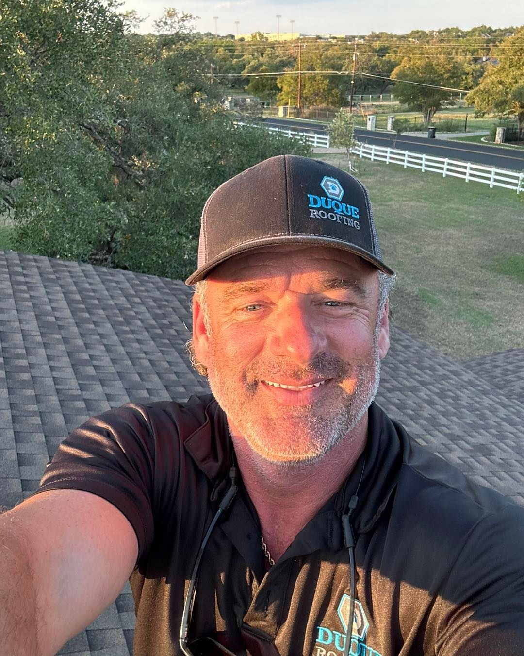 Man on a roof wearing a hat and black shirt, smiling. Outdoors, sunny setting.