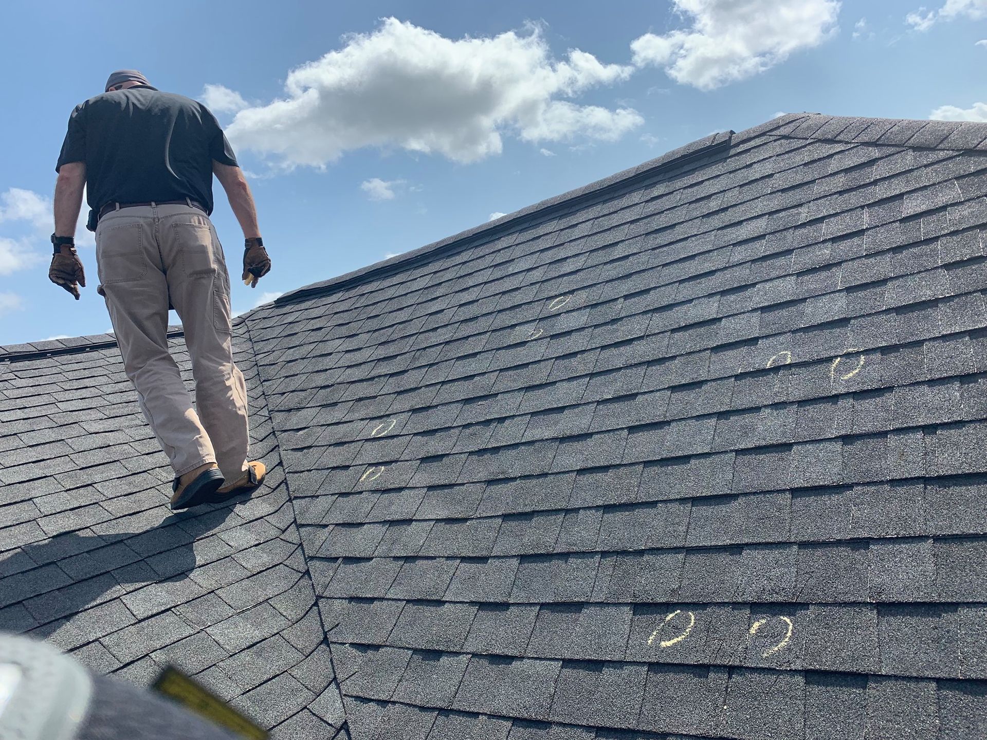 Person walking on a dark shingle roof with a blue sky background.