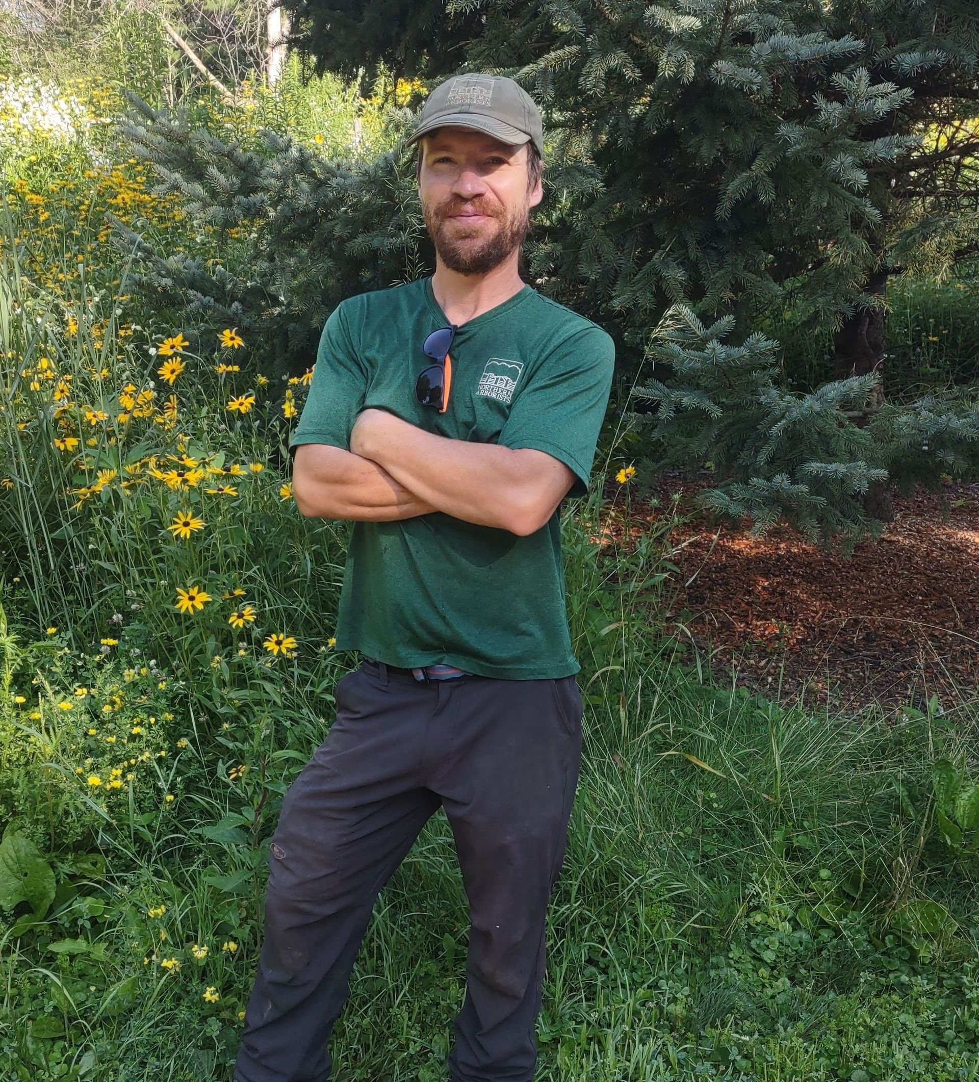 A man with a beard wearing a white shirt that says ' Northern Arborists' on it.