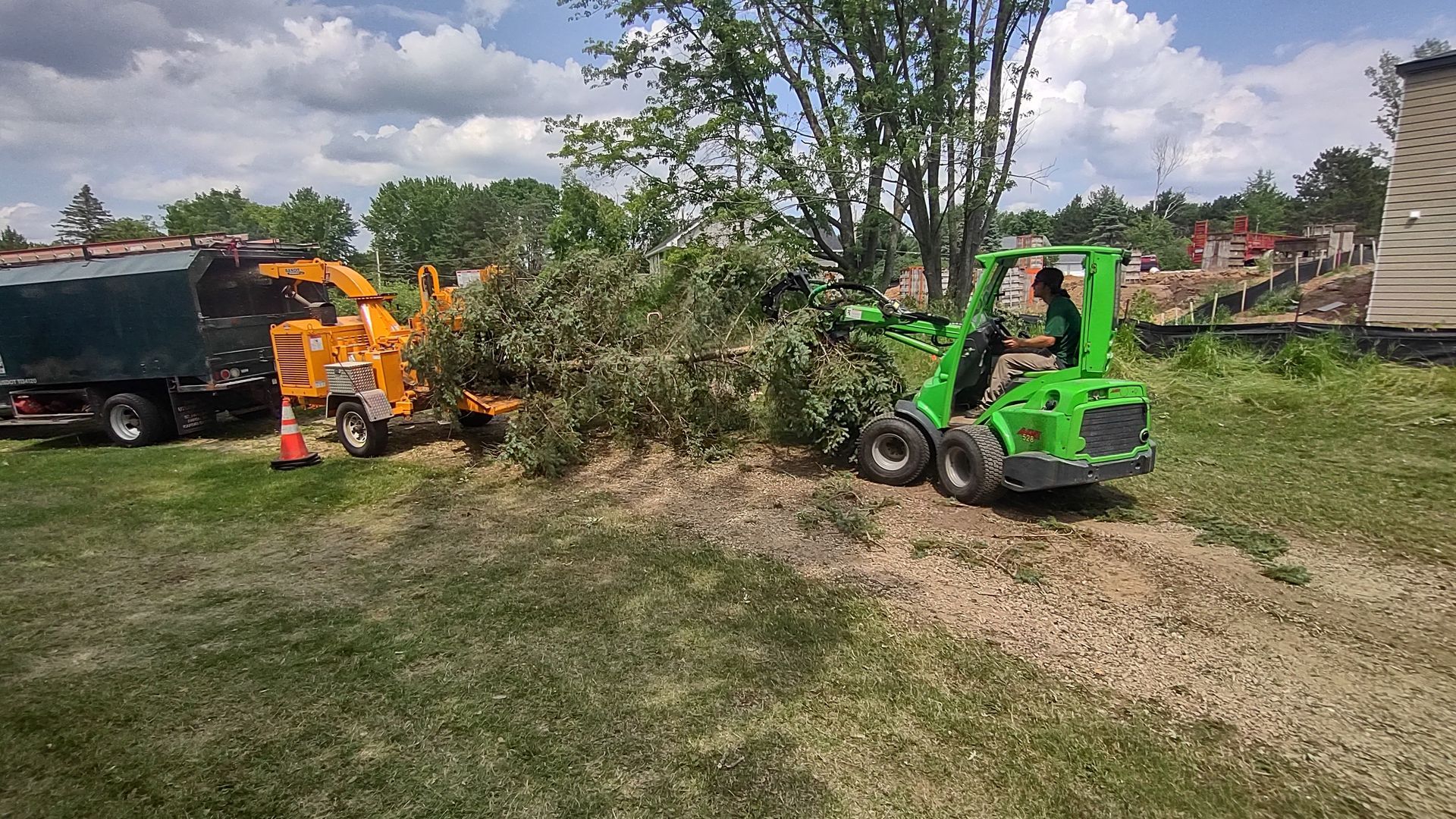 A green tractor is cutting down a tree in a yard.