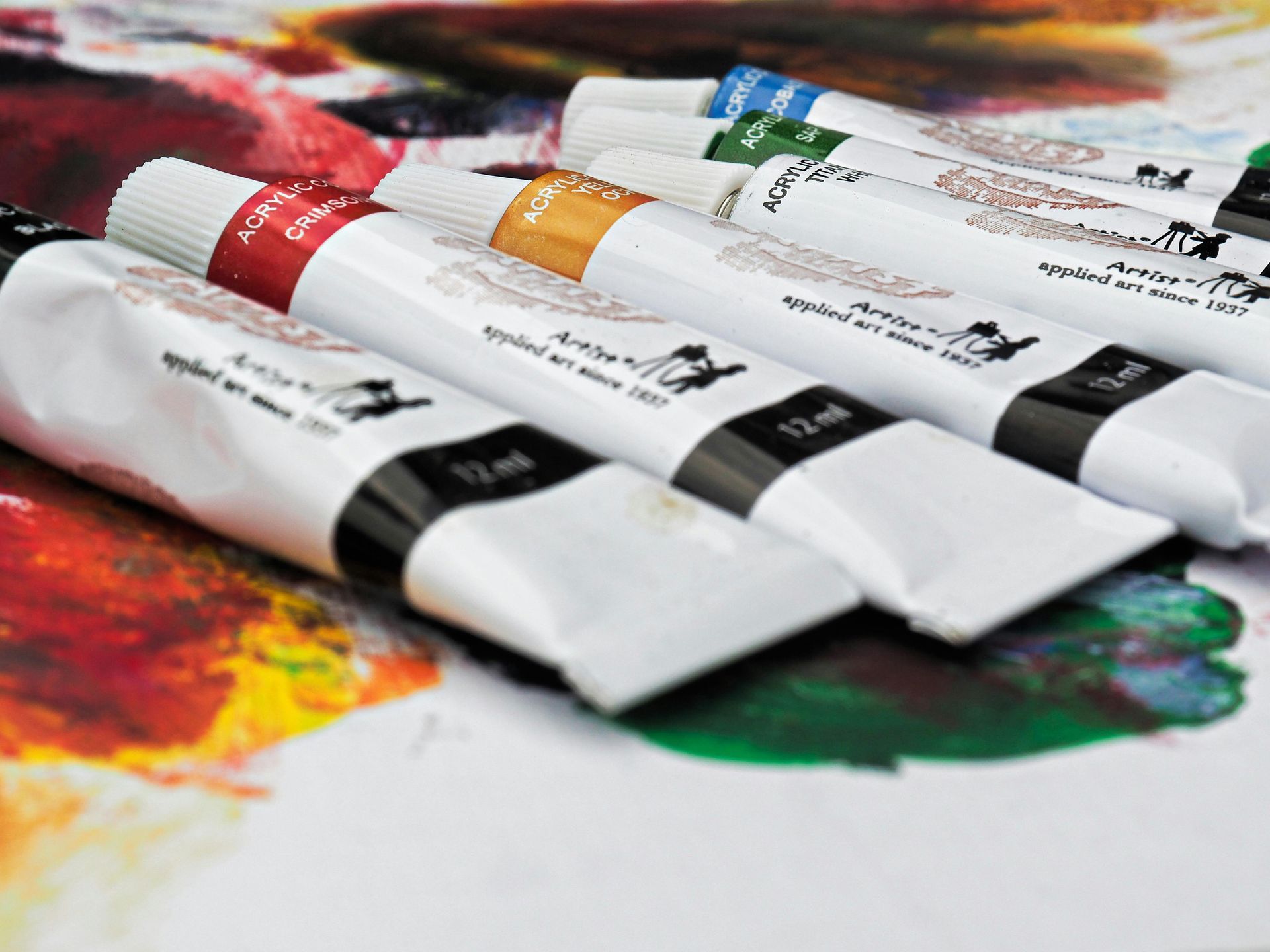 Tubes verf met rode, gele, blauwe en zwarte etiketten op een met verf bespatte ondergrond.