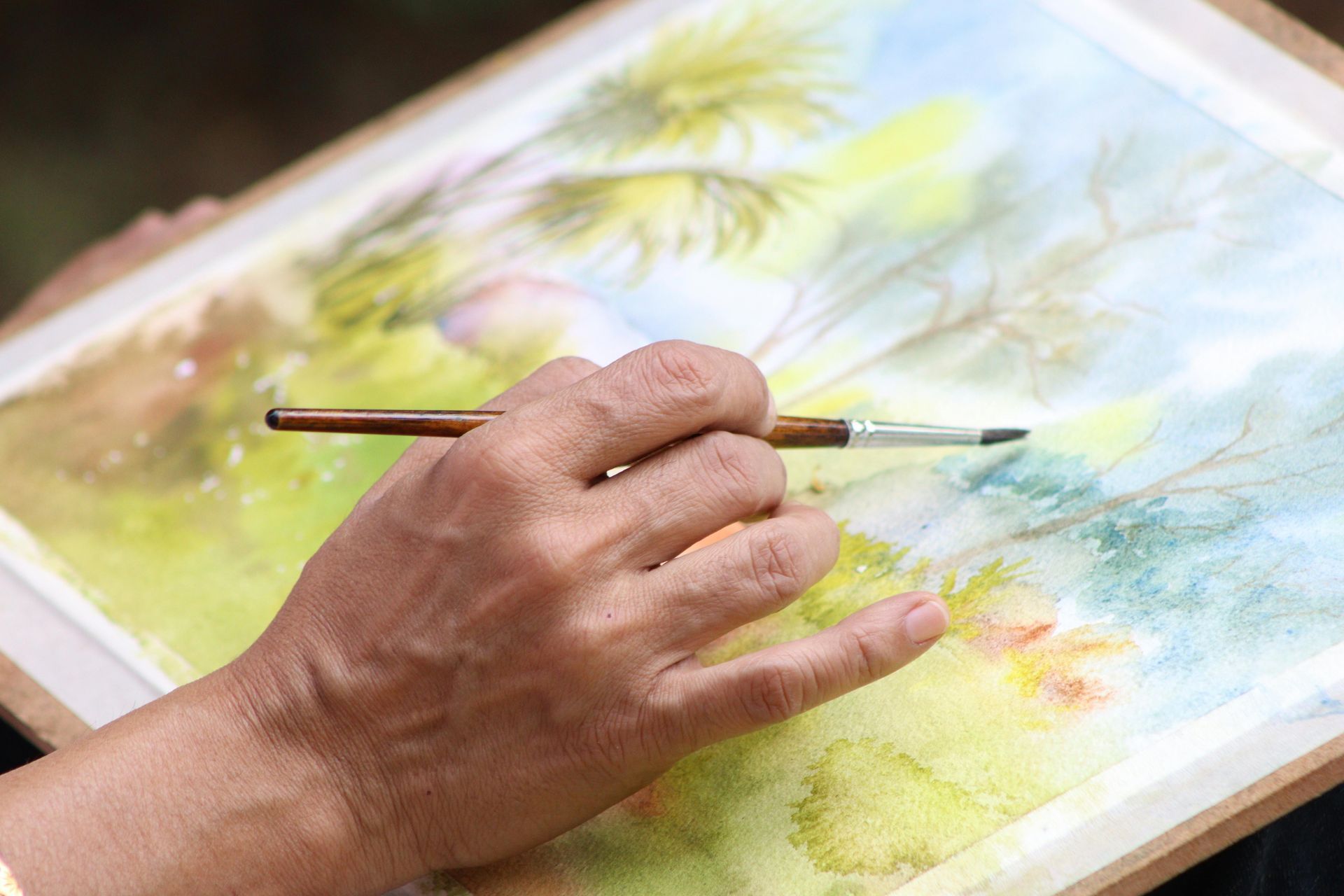 Hand die een penseel boven een kleurrijk aquarel schilderij op papier houdt.