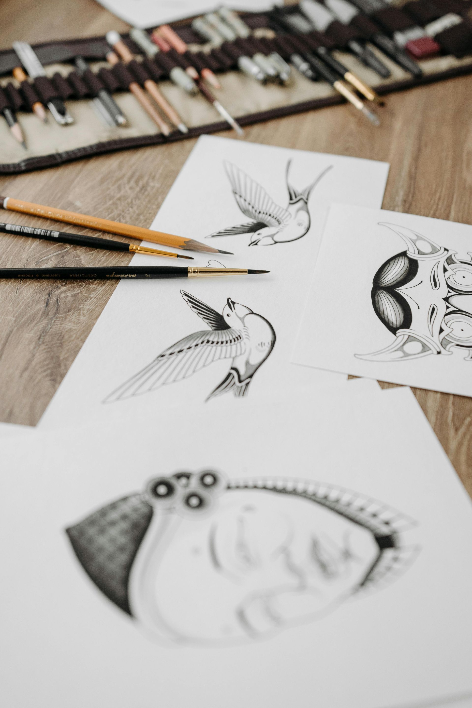Potloodschetsen van vogels en vissen op wit papier, met tekenmateriaal verspreid over een bureau.
