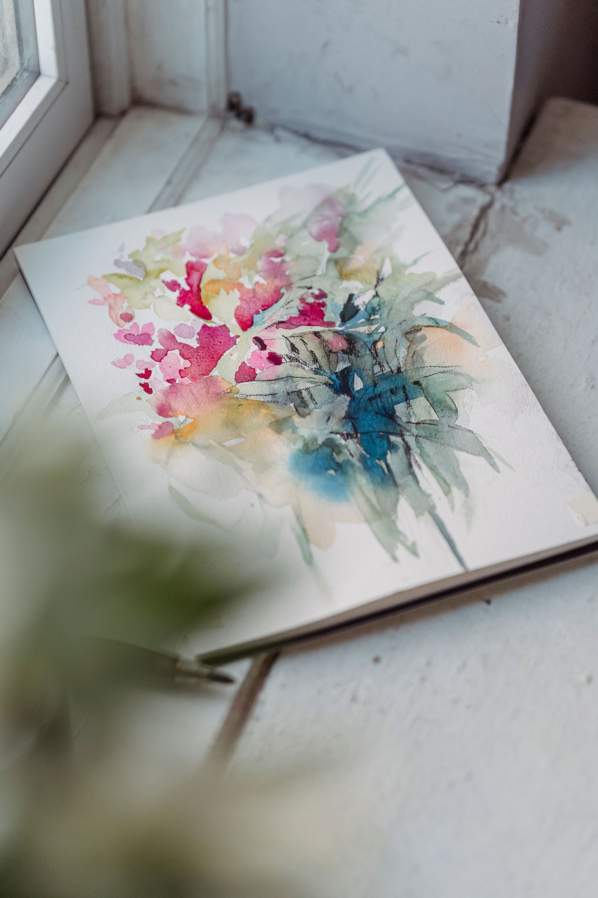 Abstracte aquarel in roze, geel en blauw op een witte tafel tegen een muur.