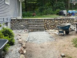 Backyard construction site: stone retaining wall, stairs, gravel pathway, wheelbarrow.