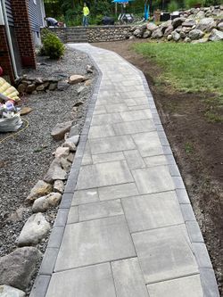 A stone walkway curves through a yard. Gray pavers are bordered by darker stones and gravel.