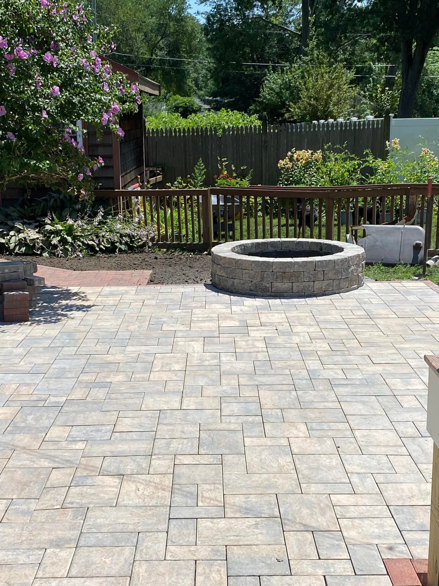 Stone patio with fire pit, fenced yard, and lush greenery.