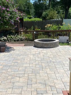 Stone patio with fire pit, fenced yard, and lush greenery.